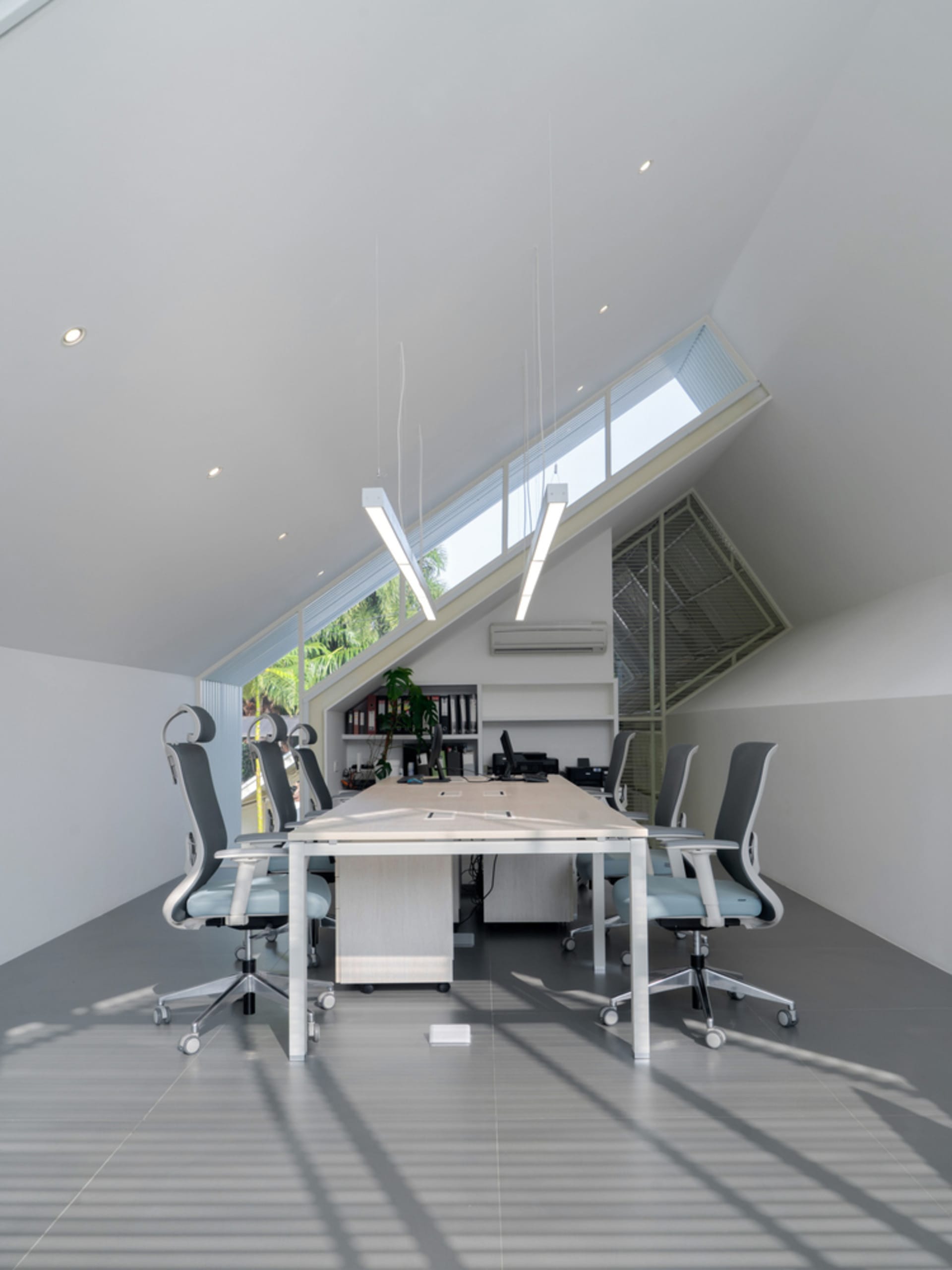 A well-lit office space with a vaulted ceiling, a dining table, chairs, and potted plants, creating a comfortable workspace