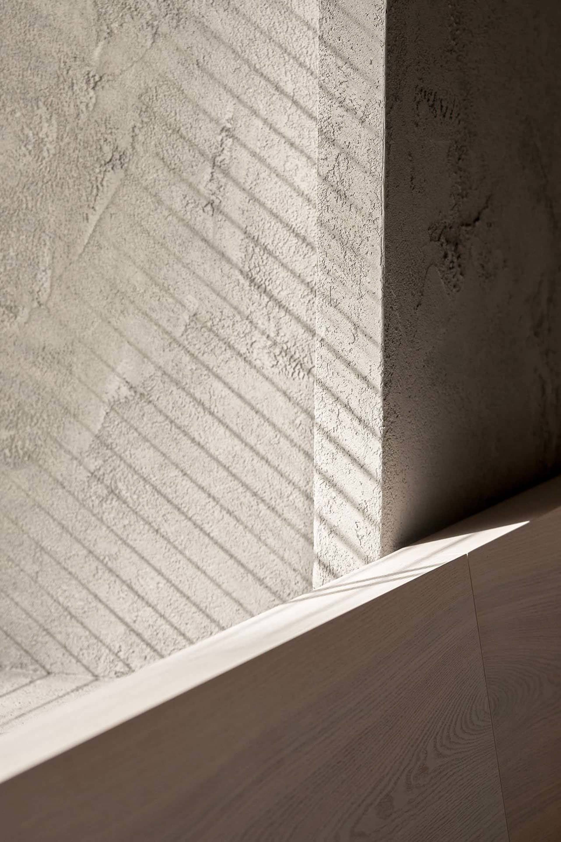 A modern indoor space with a concrete wall and a wooden surface, featuring a shadow cast on the wall, in a bright and well-lit atmosphere
