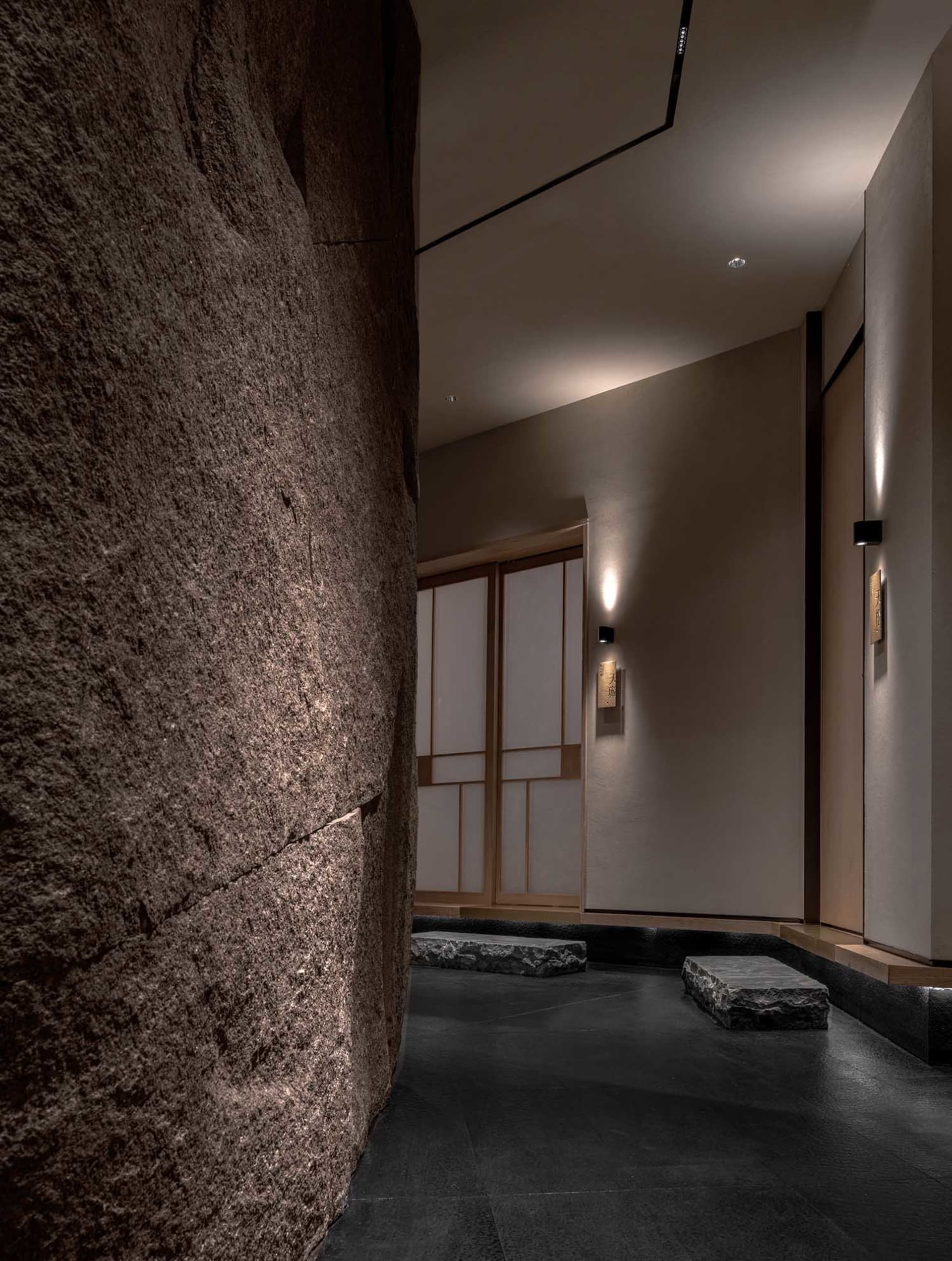Dimly lit room with a stone wall, a wooden door, two benches, and decorative bowls