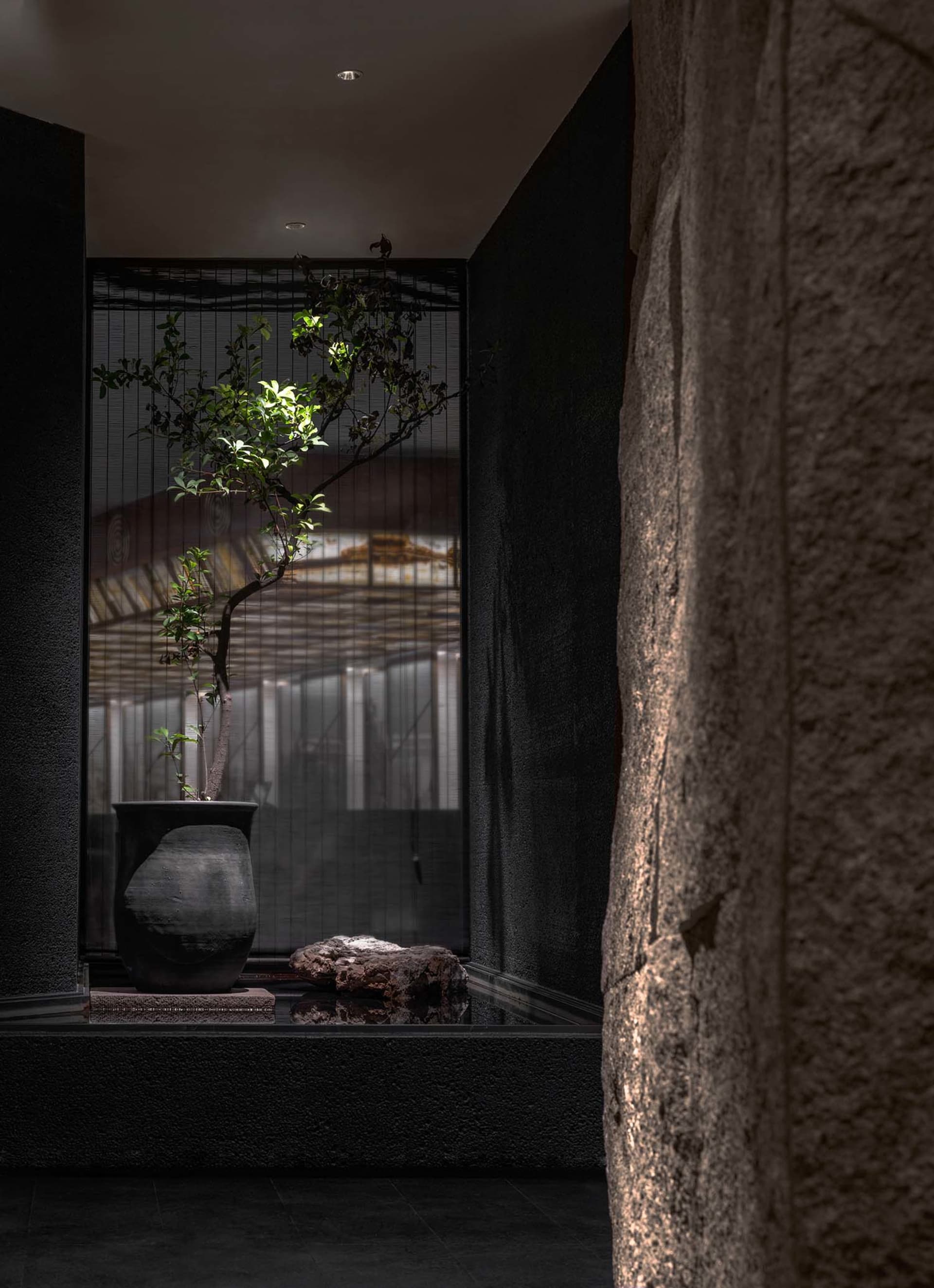 Indoor space with a black stone wall, a window, and potted plants on a table near the window, receiving sunlight