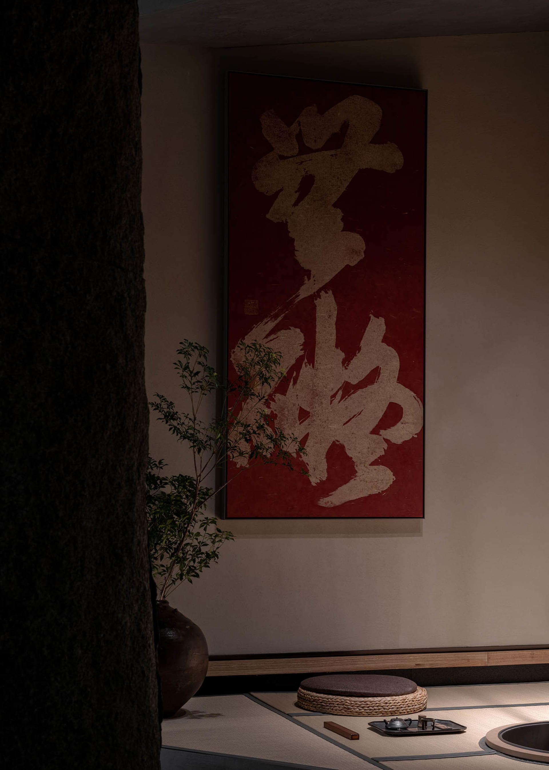 Dimly lit room with a red wall featuring Chinese characters, two potted plants, and a blend of traditional and modern design elements