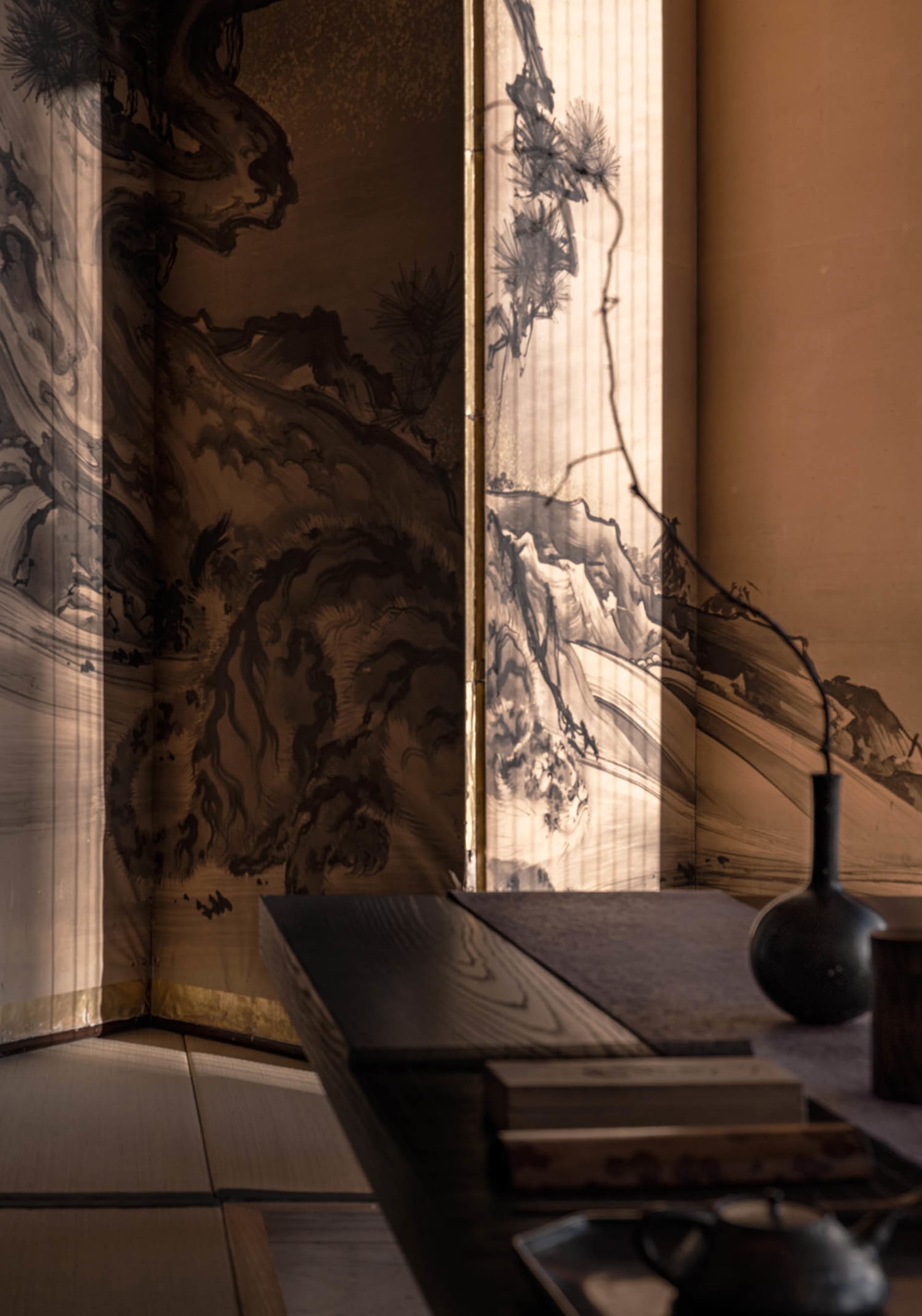 Traditional Asian living space with a wooden table, black table, and brown walls, featuring two large paintings and a warm ambiance