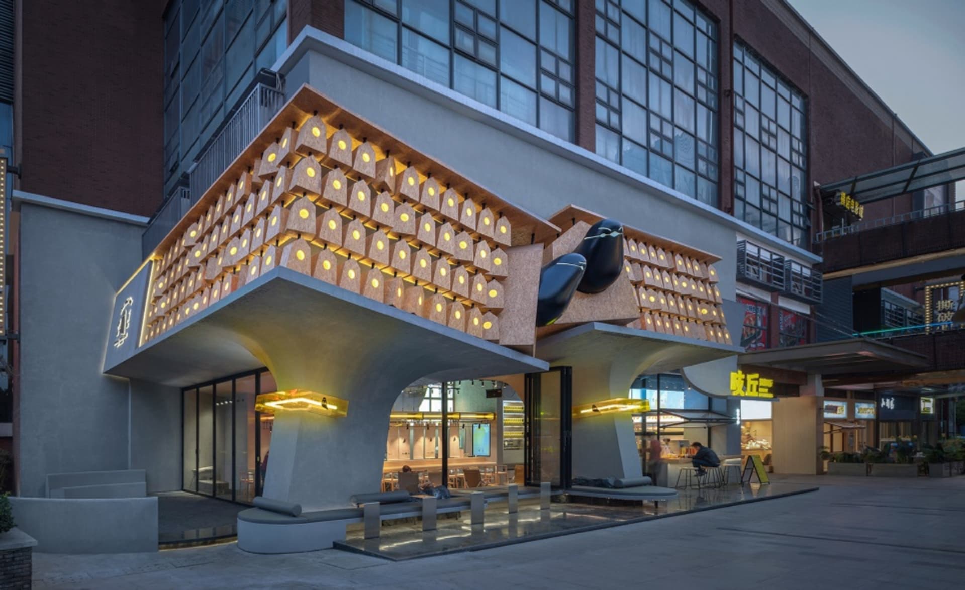 A photo of a unique boat-shaped building with a combination of wood and concrete elements, featuring several chairs and two people in a public or waiting area