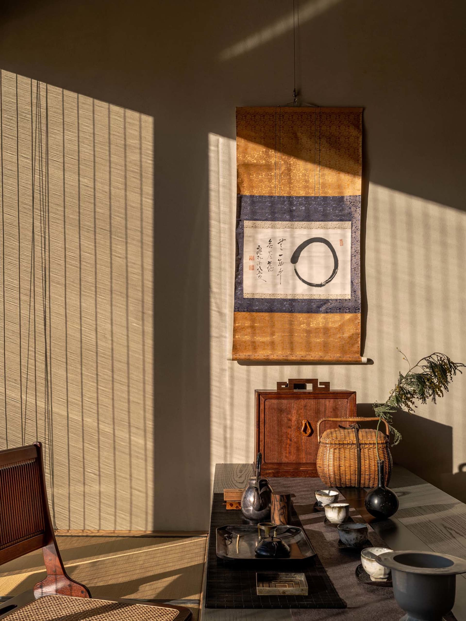 Dimly lit Asian-inspired living area with a dining table, chairs, decorative tapestry, and traditional-chic decor