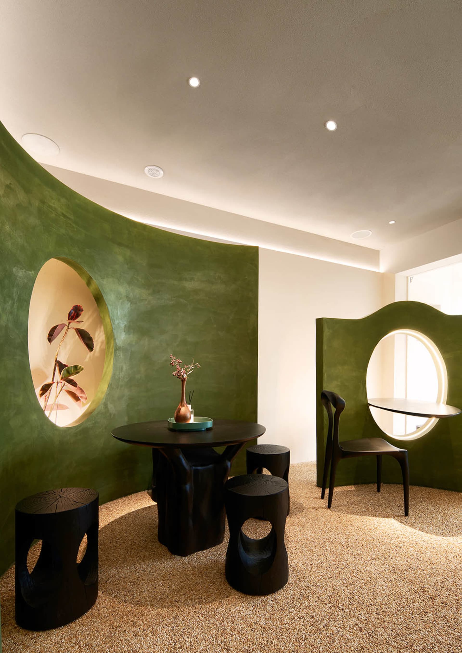 Dining area with a round table, green walls, and a potted plant, creating a cozy atmosphere