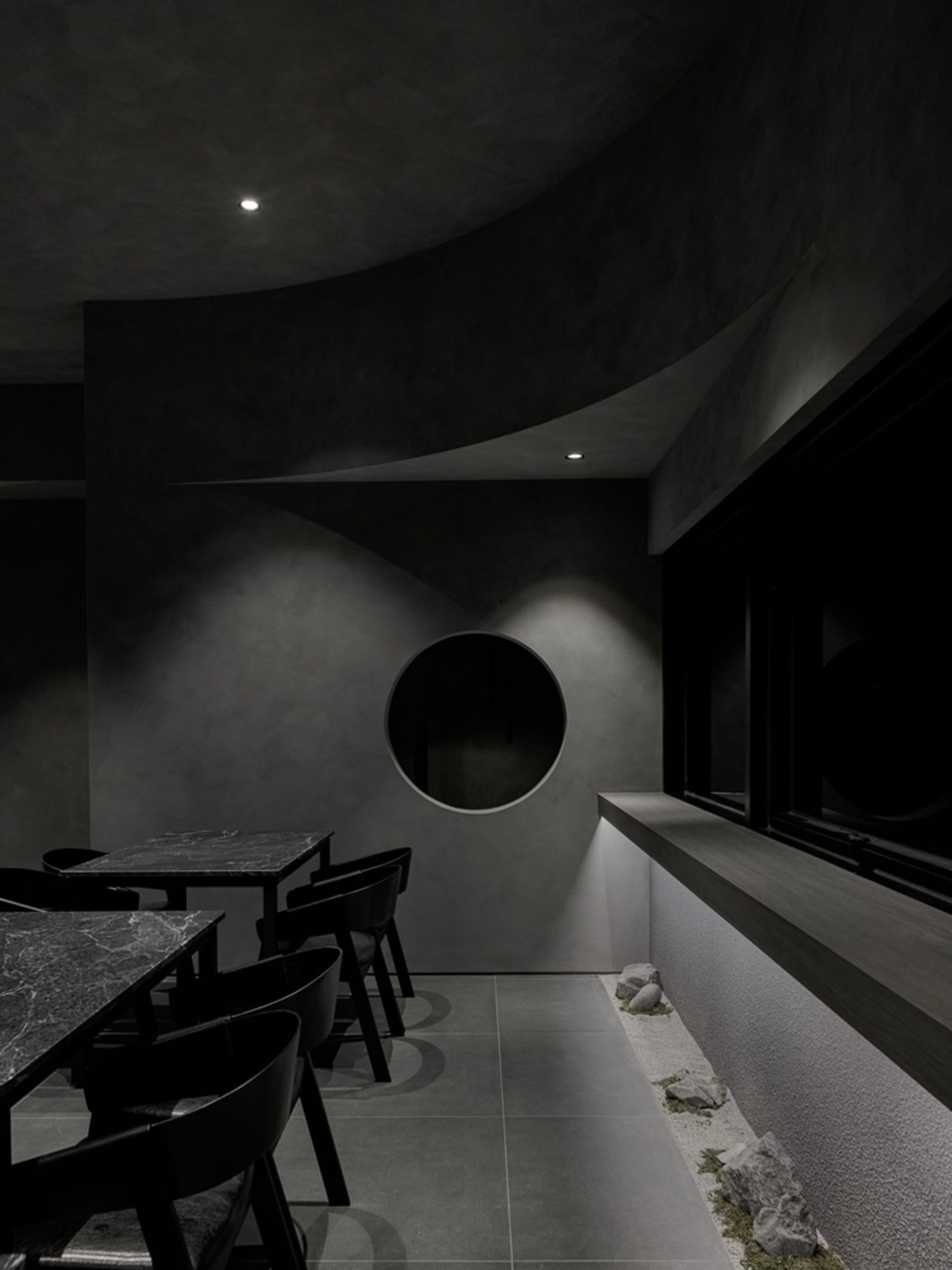 Dining area with grey stone walls, circular table, and scattered chairs, creating an inviting and comfortable atmosphere