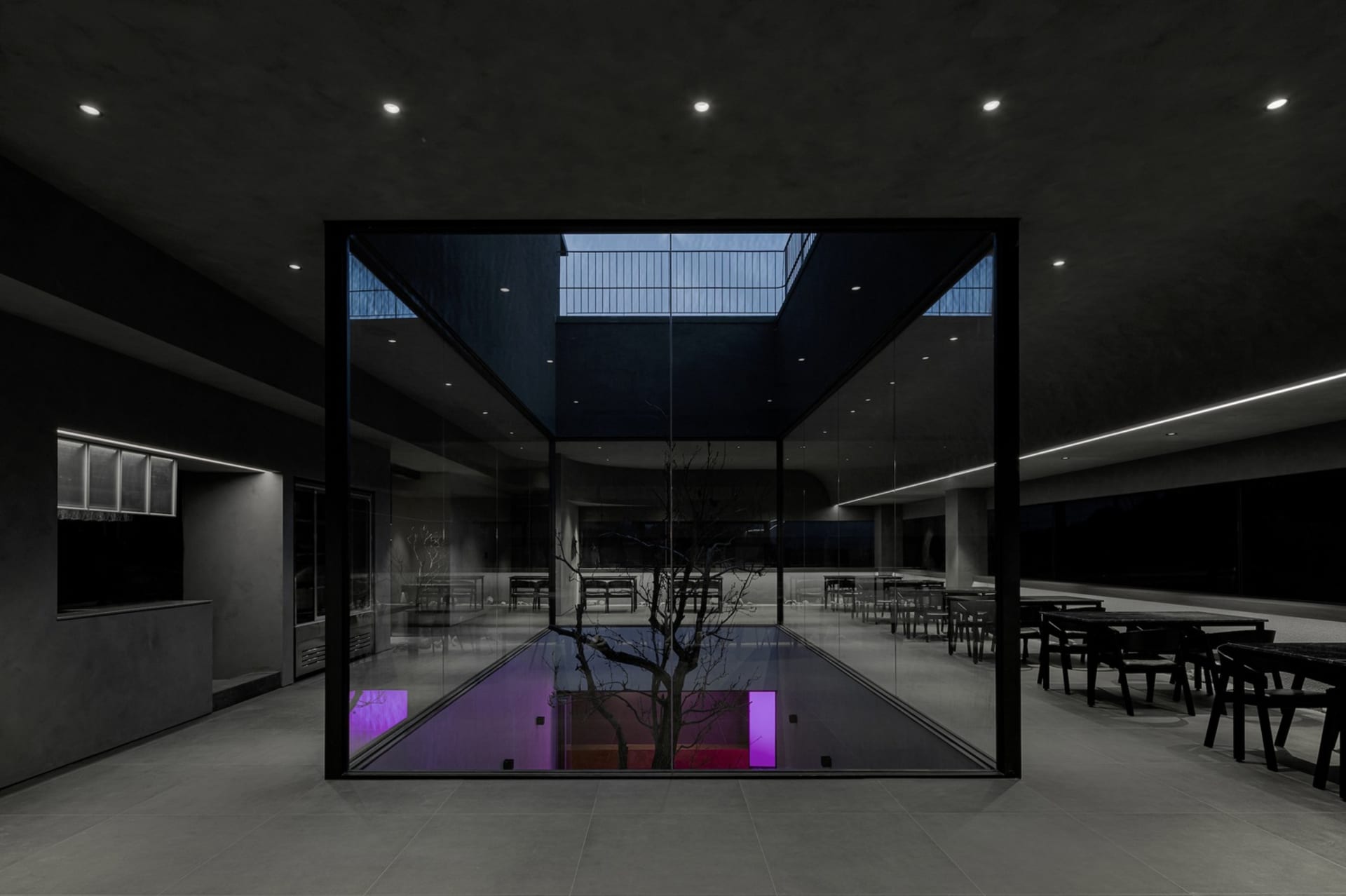 A modern indoor pool area with chairs around the pool, featuring a purple glow and well-lit surroundings