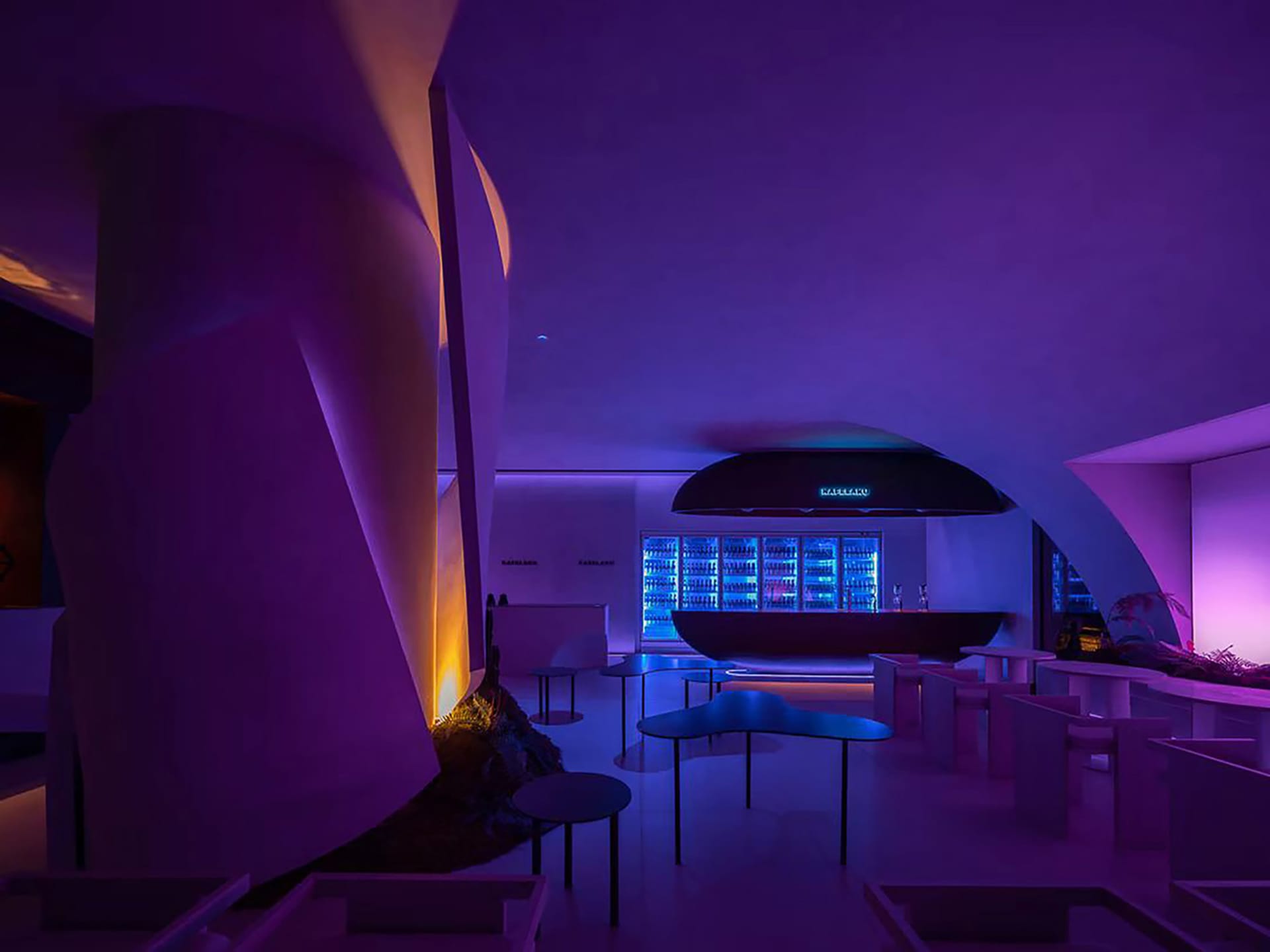 A restaurant interior with purple walls, multiple tables, chairs, and bottles on one table, creating a relaxed and inviting atmosphere
