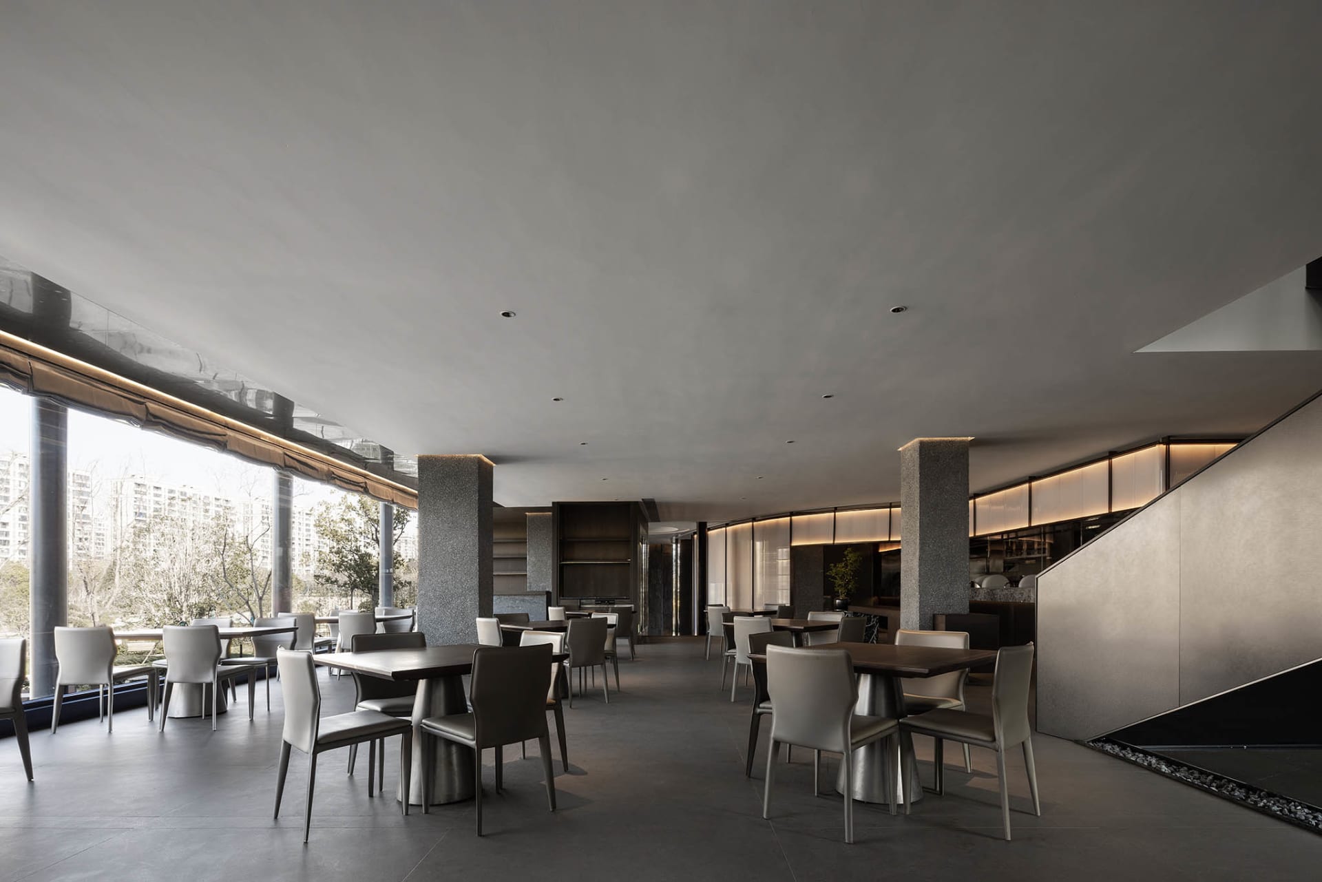 A modern restaurant interior with multiple dining tables and chairs, gray walls, and a spacious atmosphere