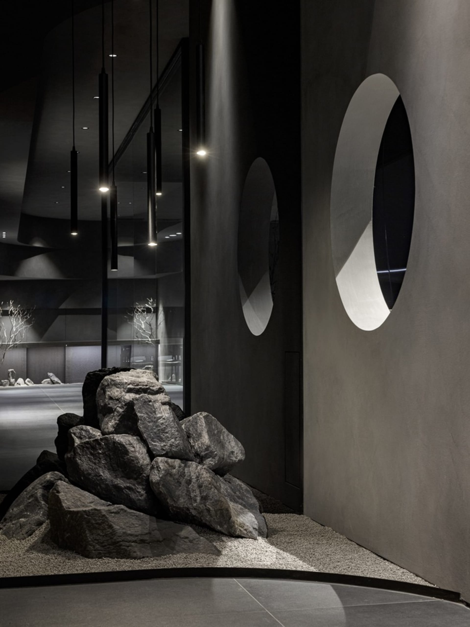 A modern living and dining space featuring a large rock in the center surrounded by other rocks, with two dining tables and a stylish atmosphere