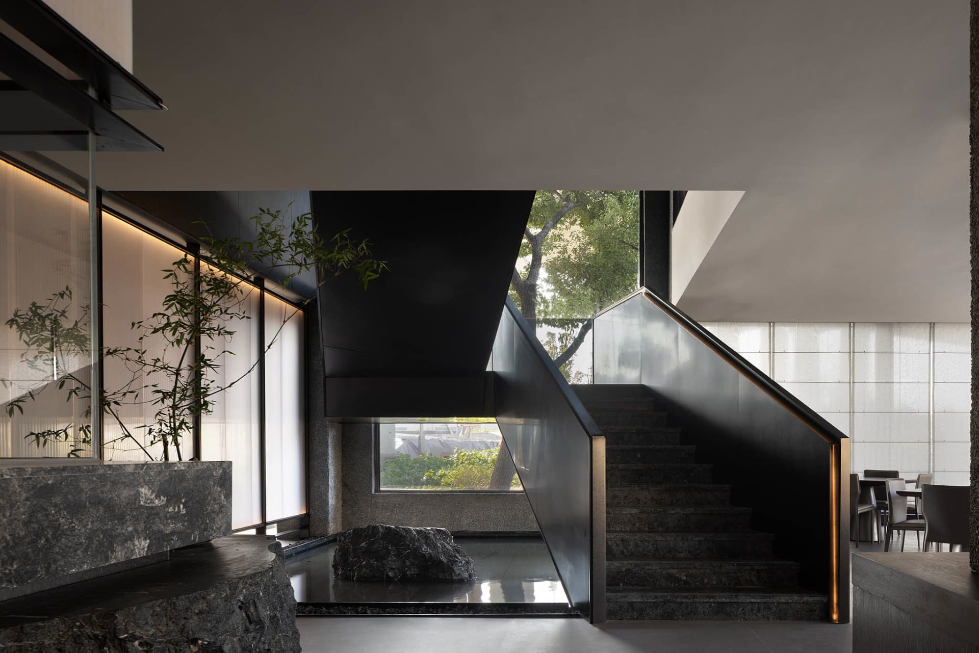 A modern staircase in a contemporary building with black walls, surrounded by two potted plants, creating a balanced and inviting atmosphere