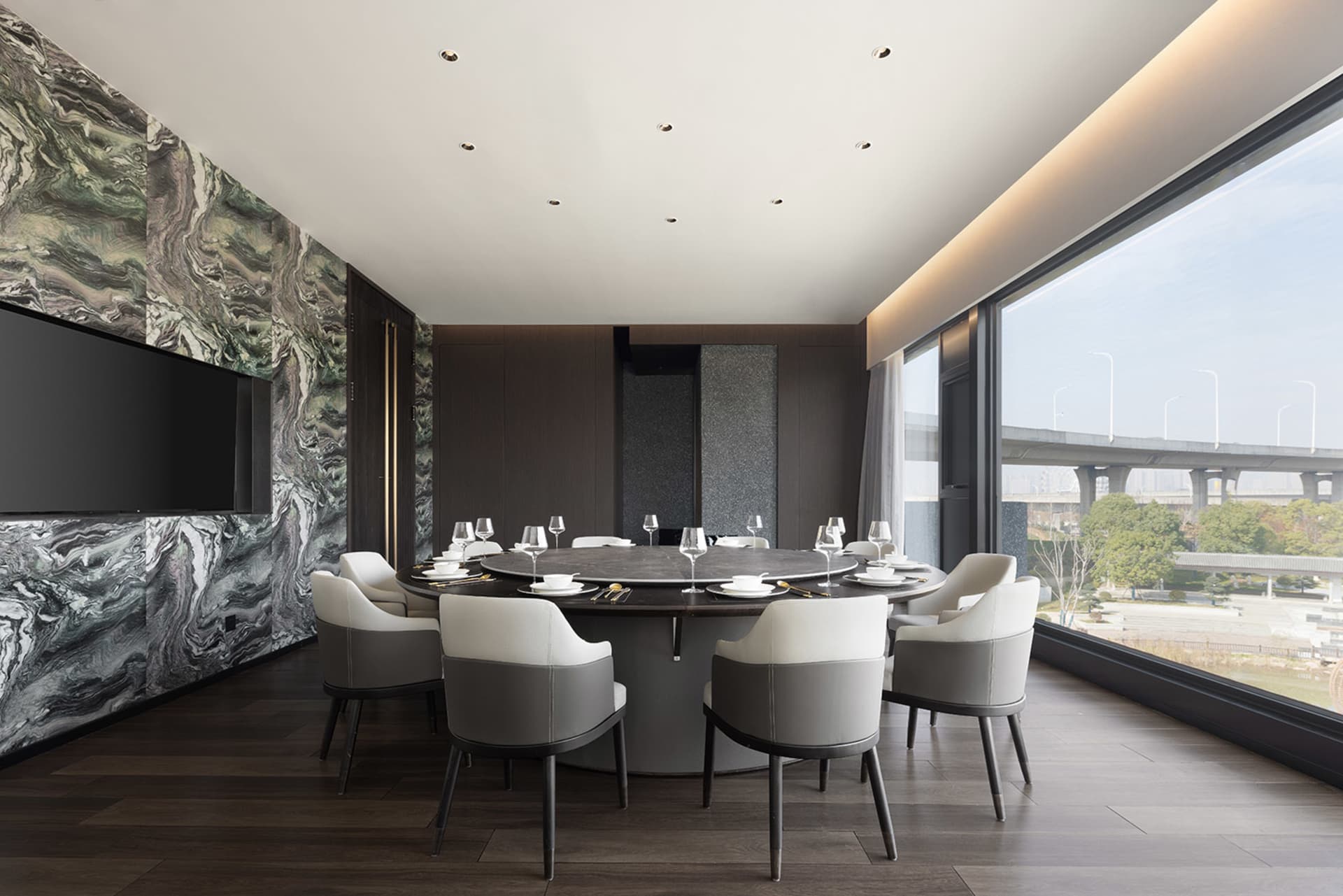 A modern dining area with a round table, chairs, and fine dining setup, set against a wood-floored background