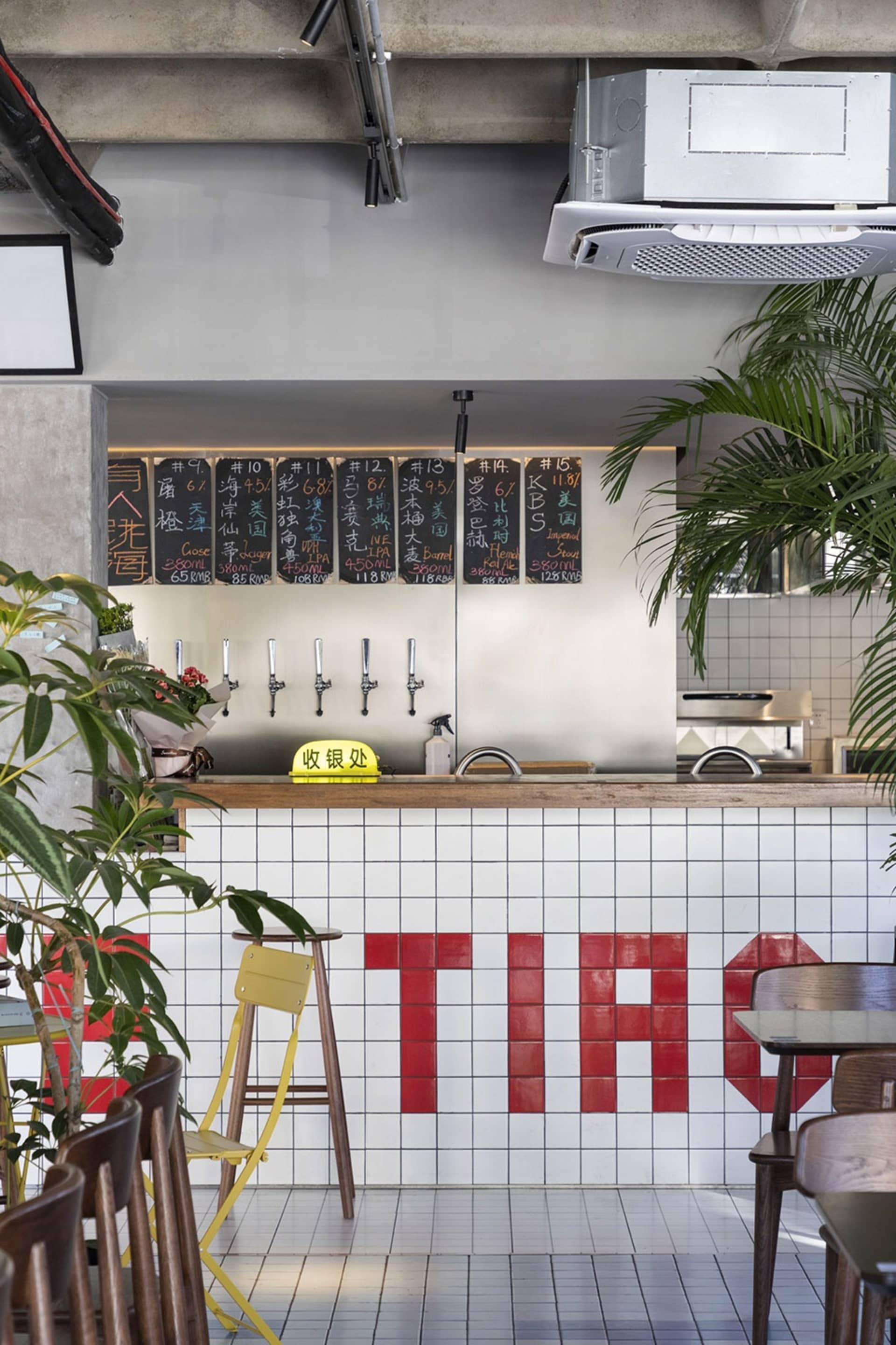 Casual restaurant interior with a bar area, dining tables, potted plants, and signs on the walls
