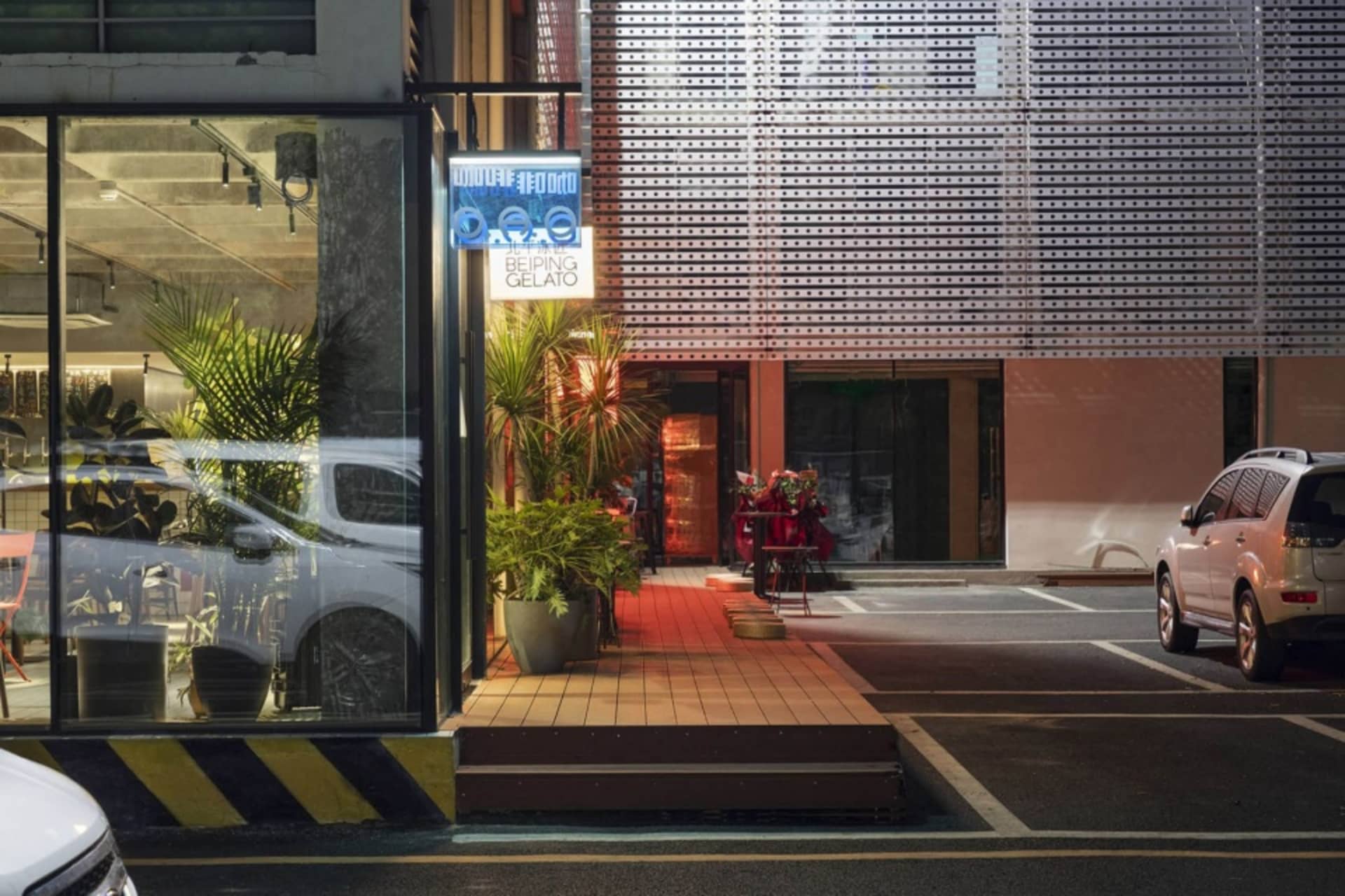 夜晚建築外觀，停有兩輛車及盆栽植物，在黑暗背景下被照亮