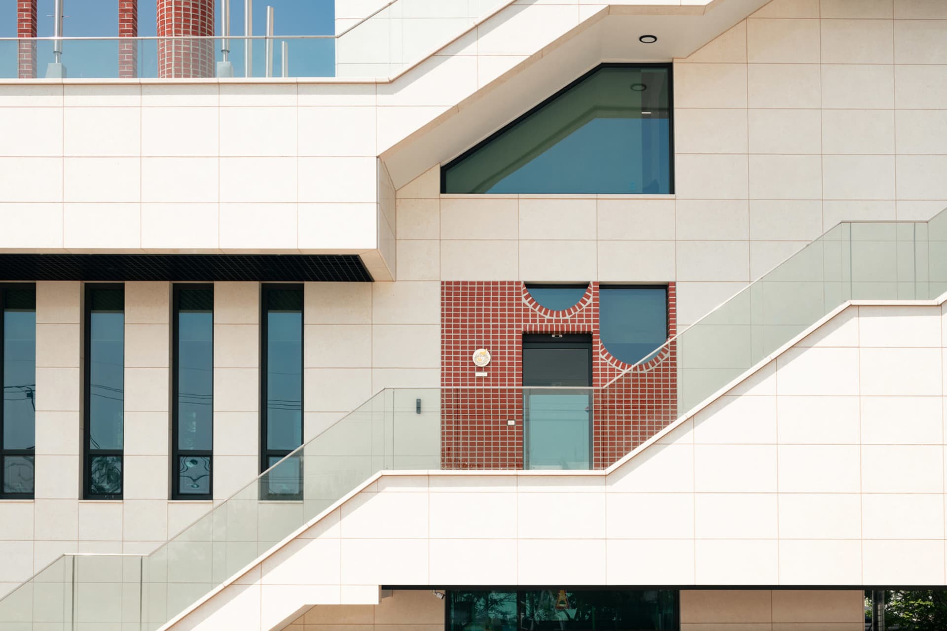 A multi-level building with white walls and red brick elements, featuring stairs and a mix of residential and commercial spaces