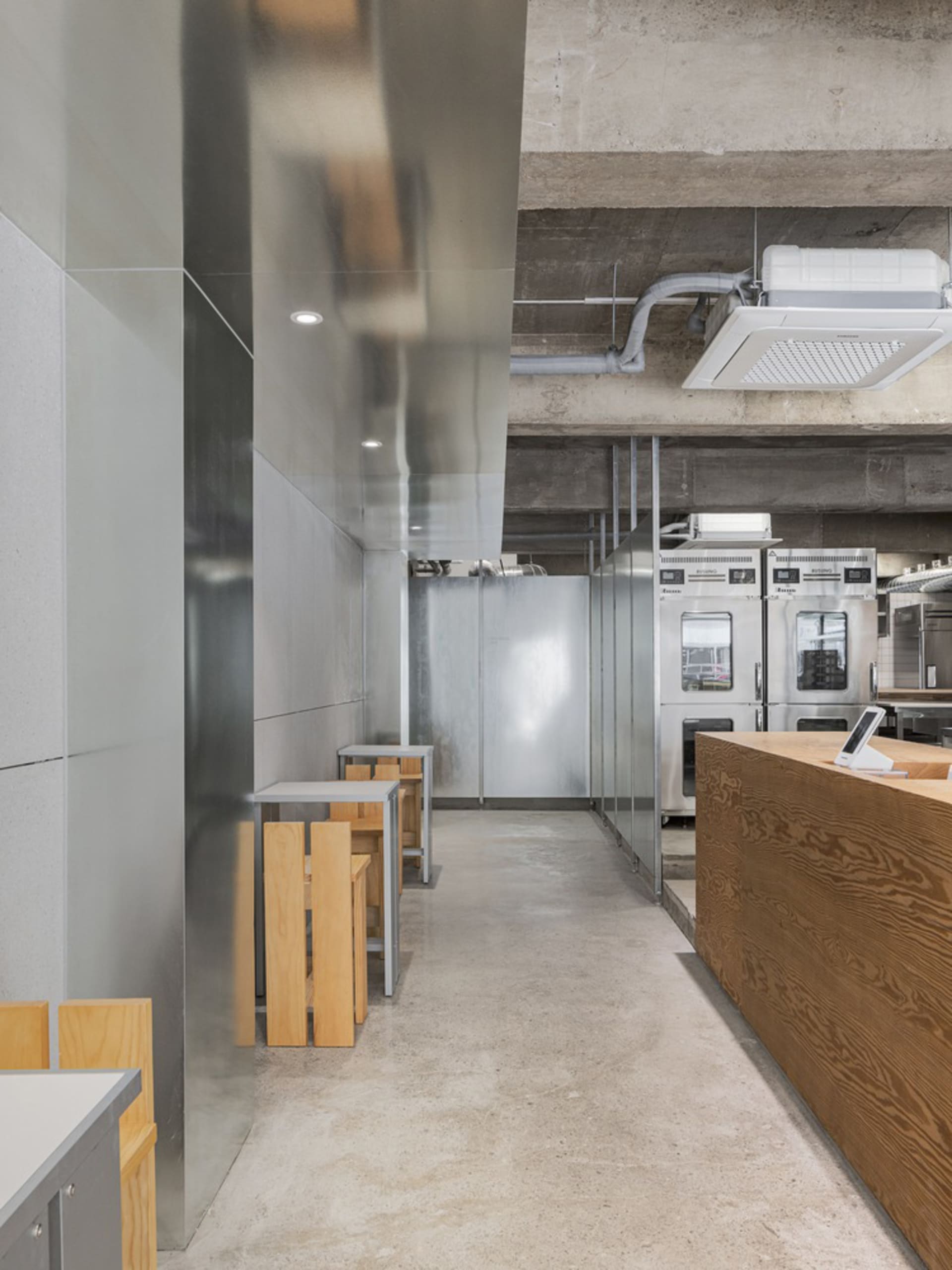 Empty restaurant interior with a cement floor and walls, featuring wooden tables and chairs in a clean and well-organized atmosphere