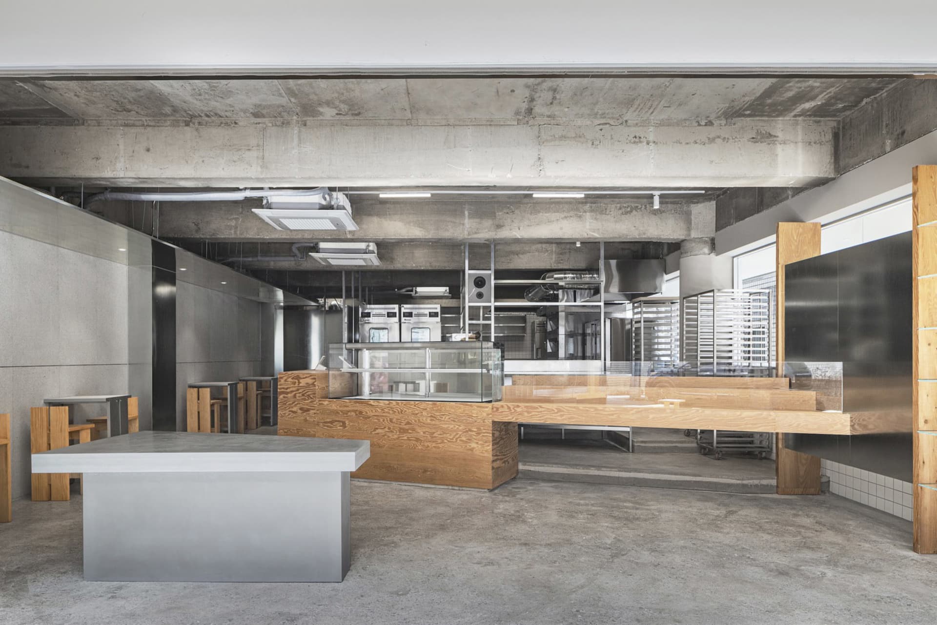Industrial kitchen with a large wooden countertop, sink, ovens, and refrigerator, giving off a modern and sleek vibe