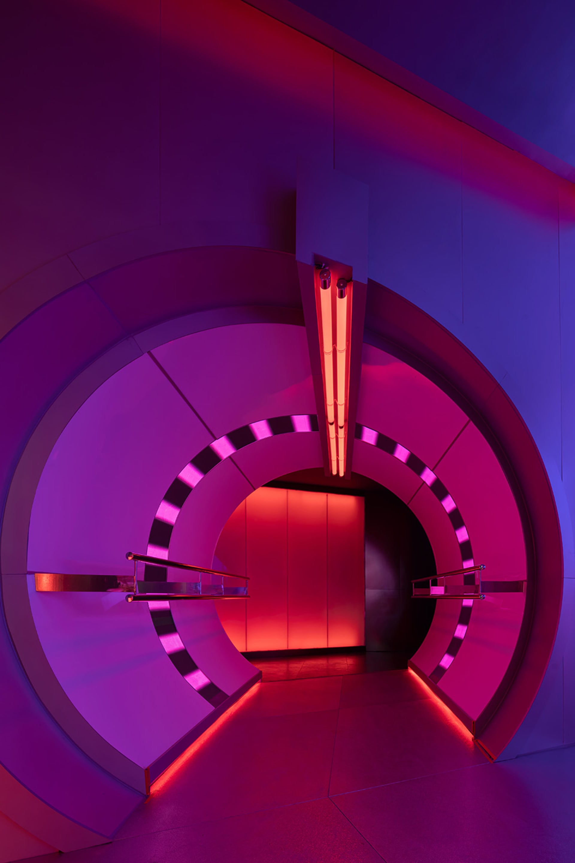A futuristic interior space with a spiral staircase, pink and purple walls, and red lights on the staircase
