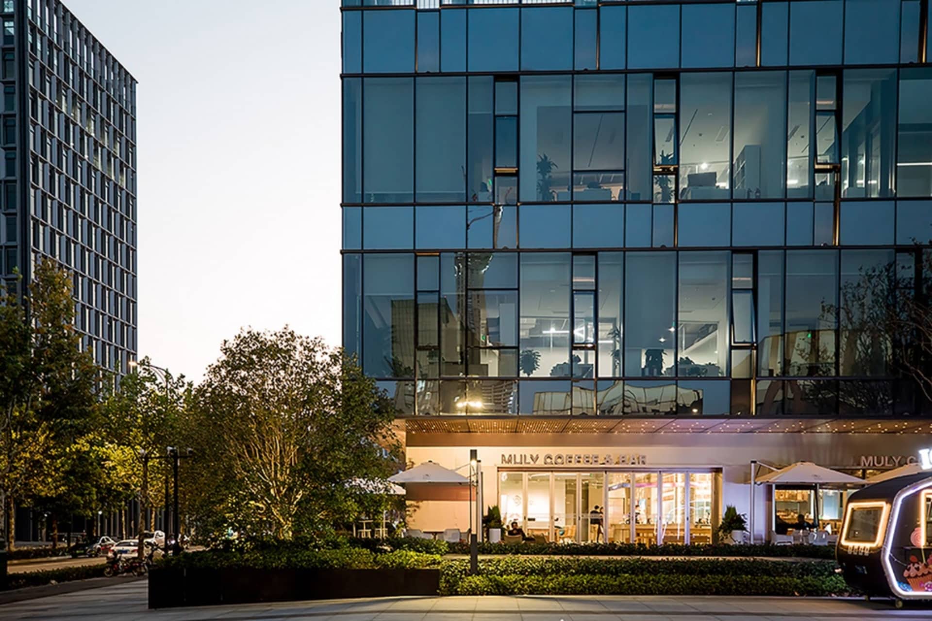 A modern building with a glass facade, featuring many windows and a contemporary design, surrounded by potted plants in an urban environment