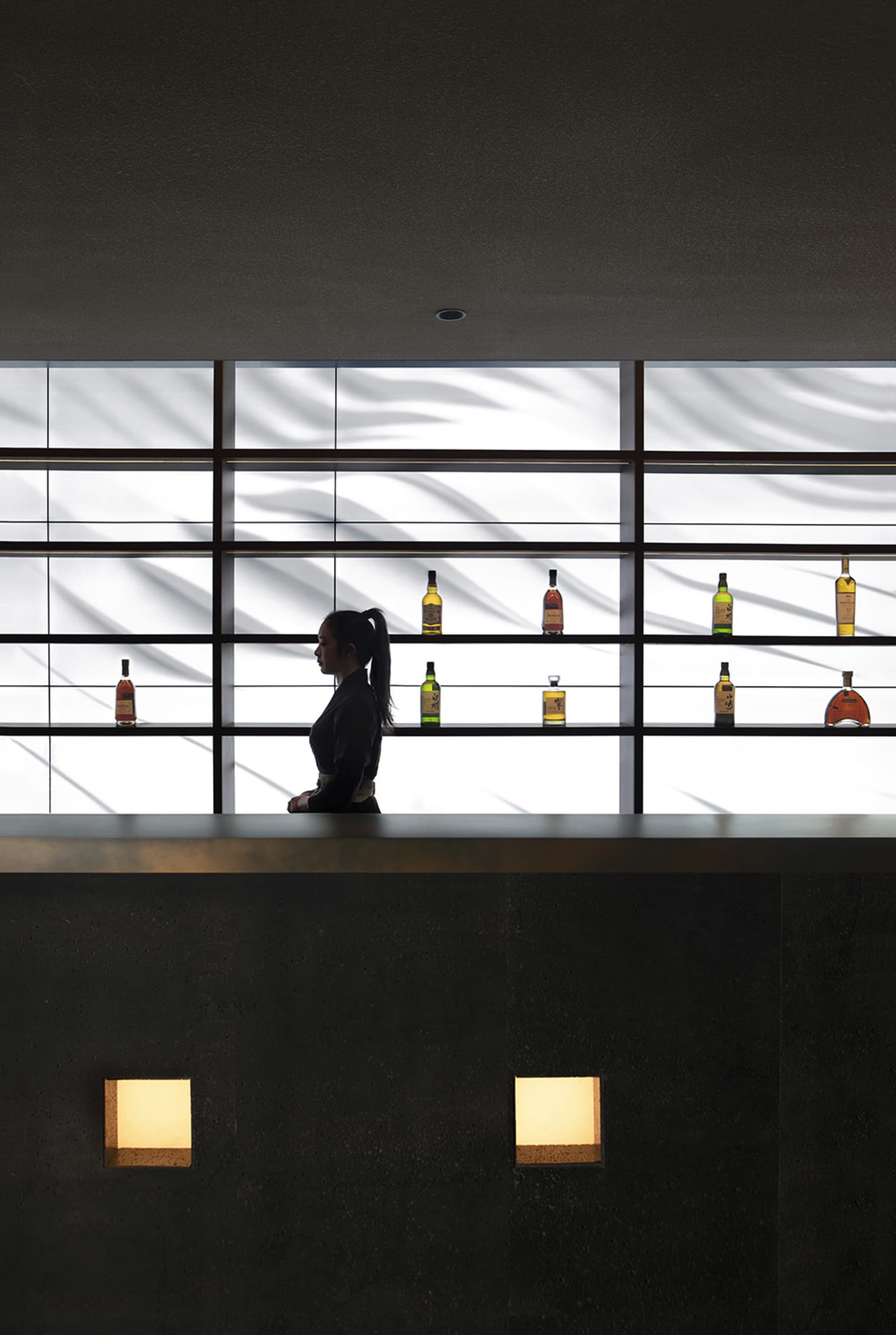 A woman works behind a bar with a vast array of liquor bottles, suggesting a lively social gathering or event