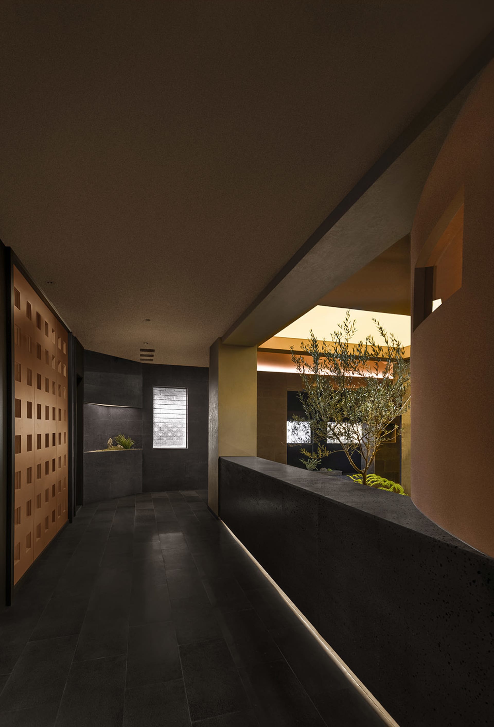 A cozy hallway with a black tile floor, sunlight, and two potted plants, with a bench along the wall