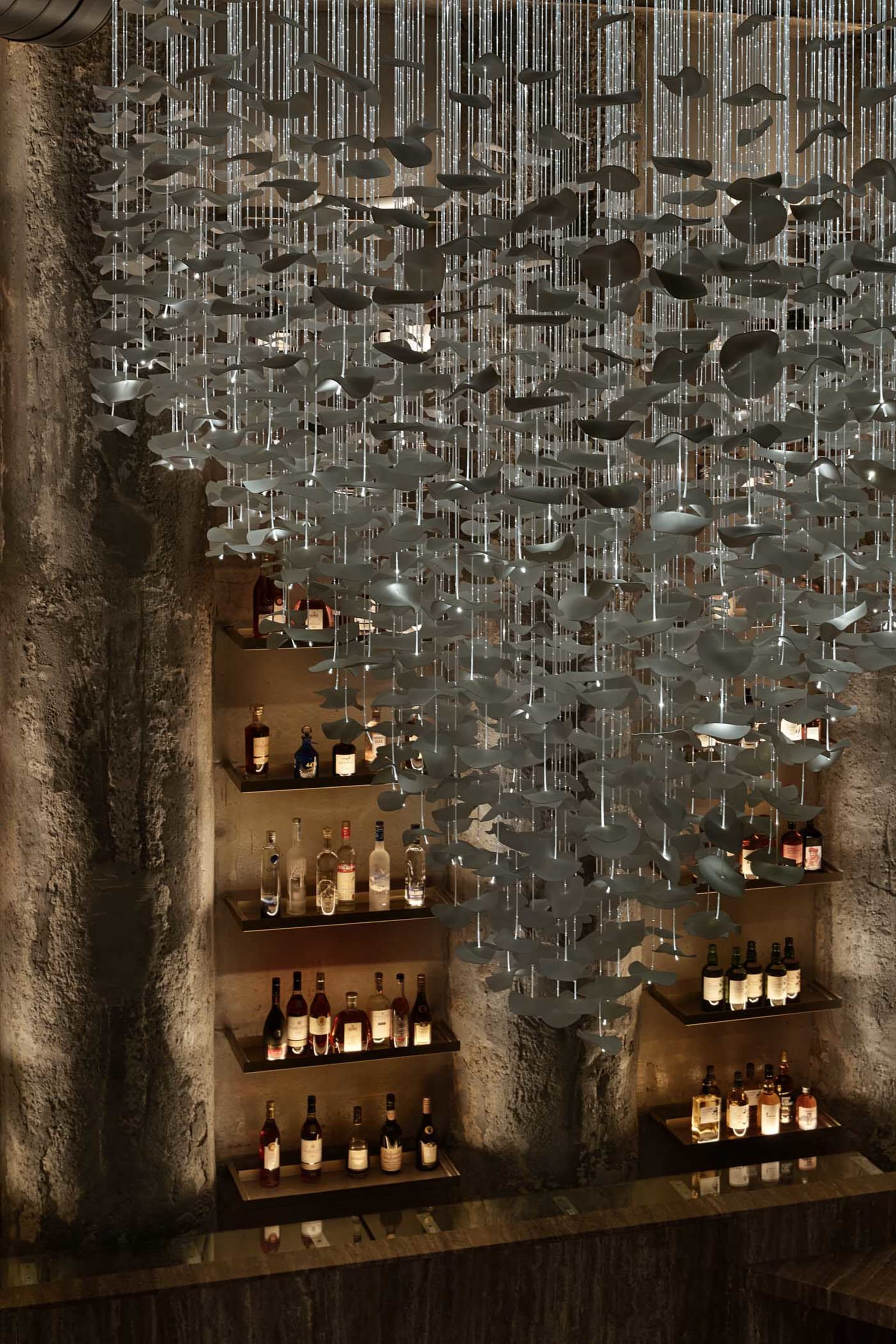 Cozy bar area with stone walls, wine glasses hanging from the ceiling, and a variety of bottles on shelves, creating a warm and inviting atmosphere