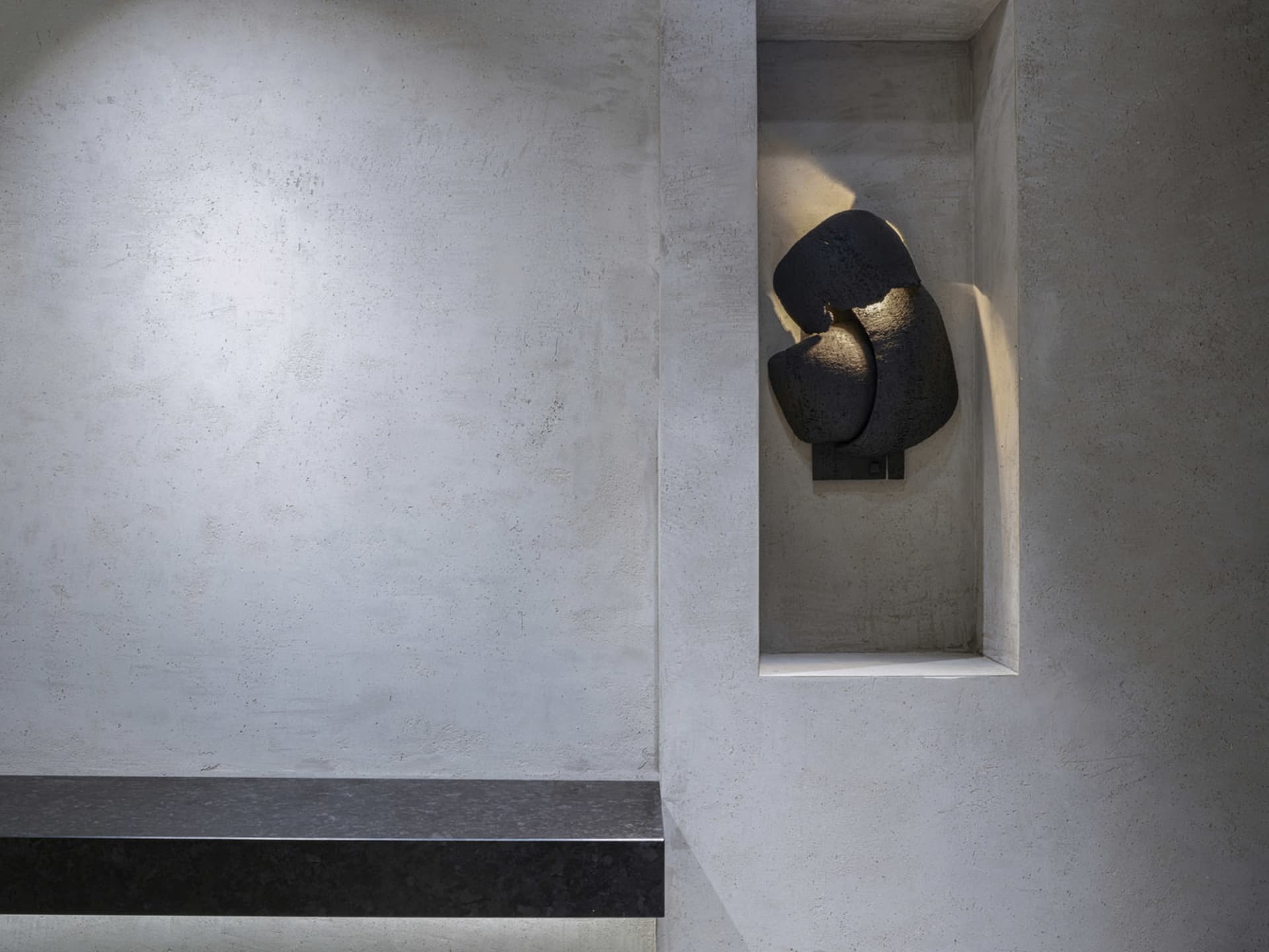 A stone bench sits in front of a wall with a unique design element, set in a contemporary and stylish space with natural materials