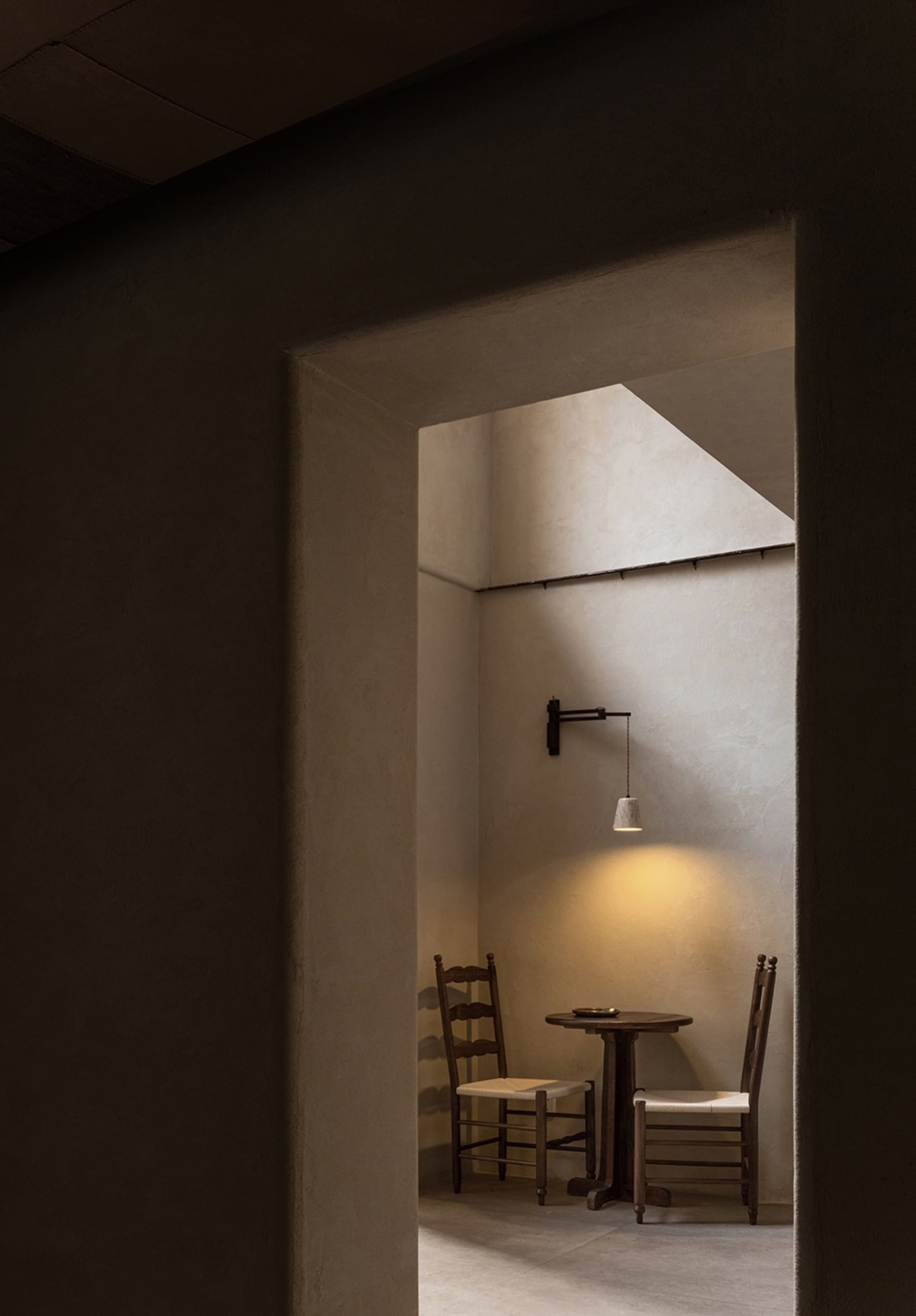 Dimly lit dining room with a concrete wall, a dining table, and two chairs, creating a cozy atmosphere