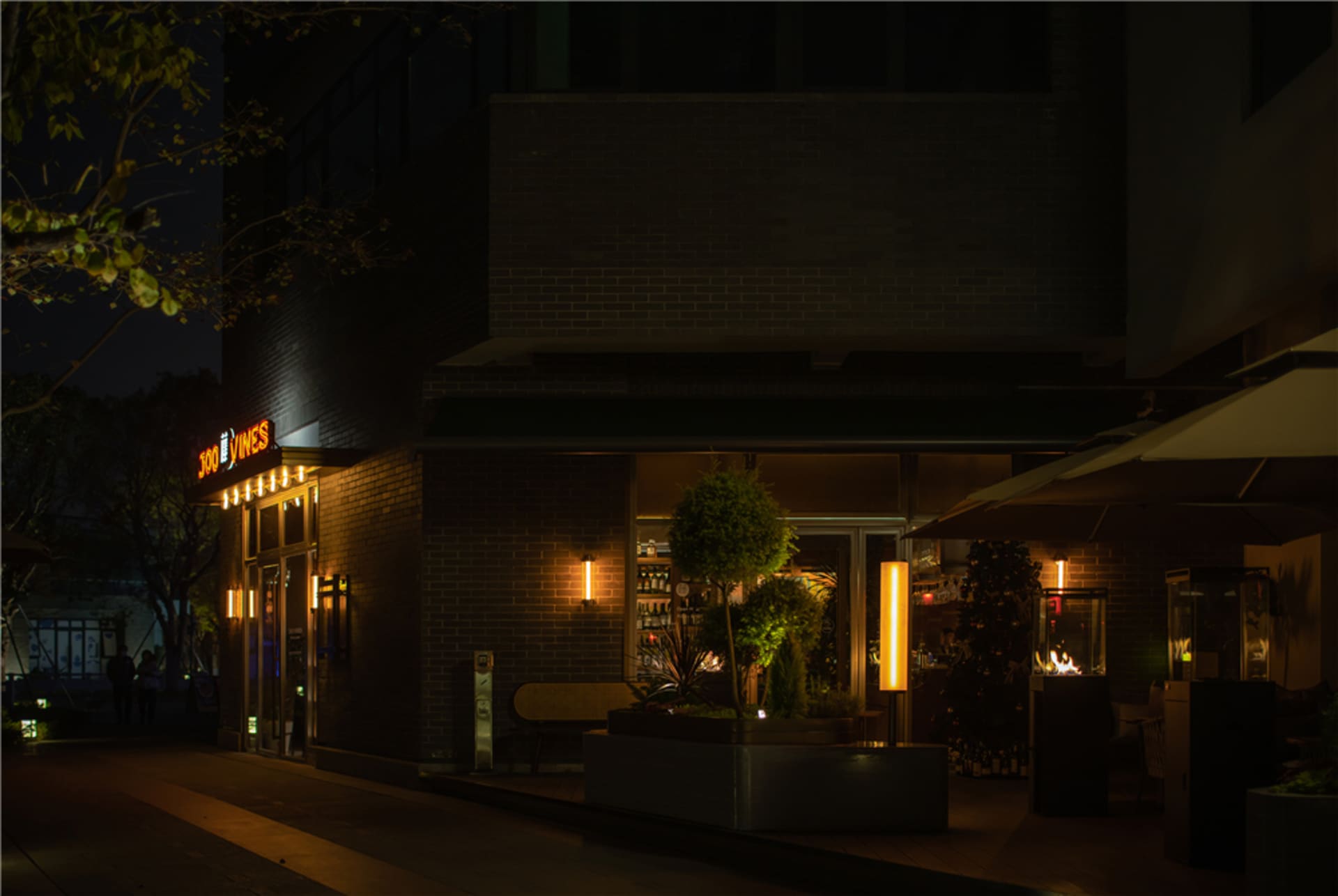 夜晚溫馨吸引人的磚牆外觀餐廳，搭配大樹與盆栽