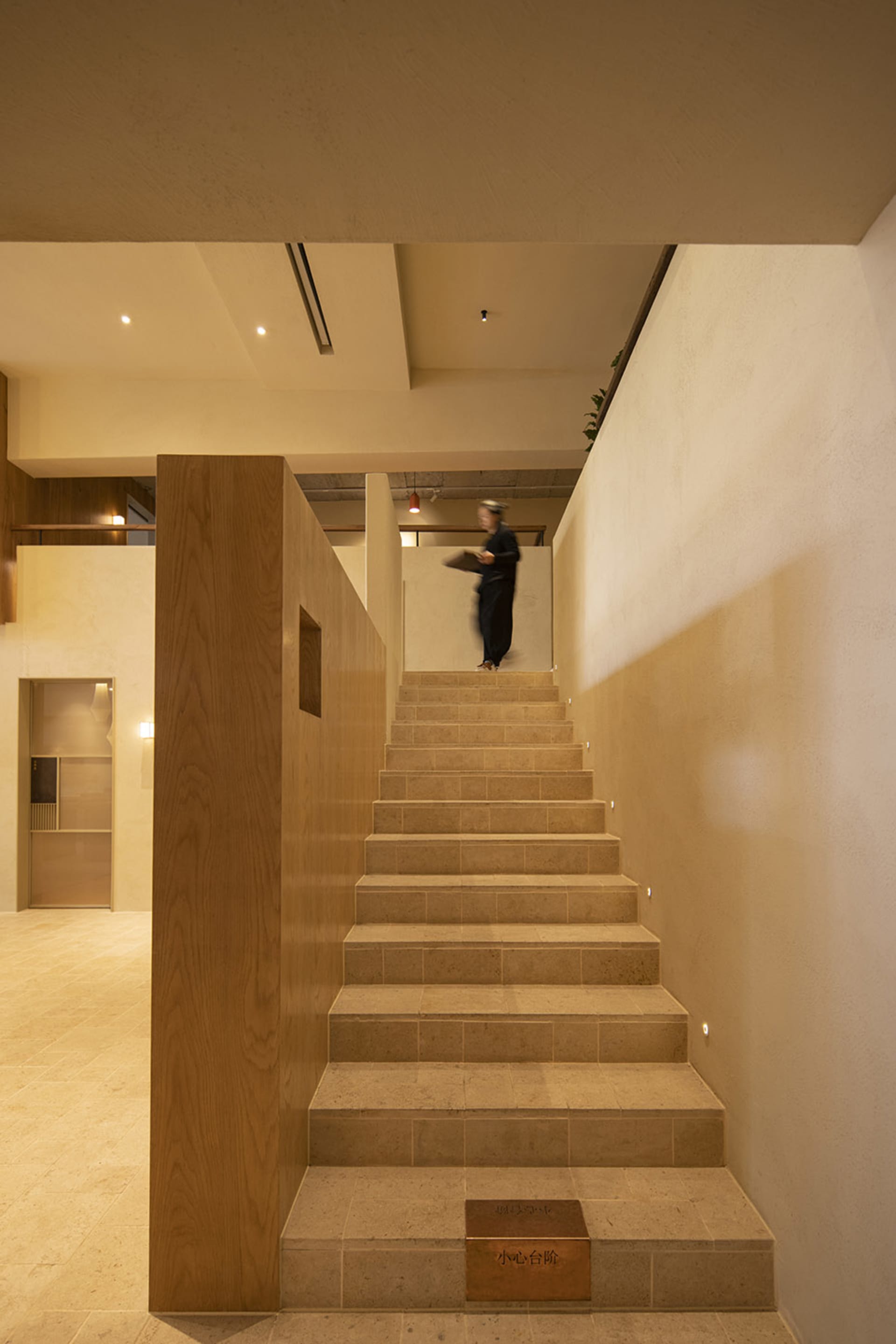 A person stands on the first step of a wooden staircase in a calm and inviting interior space