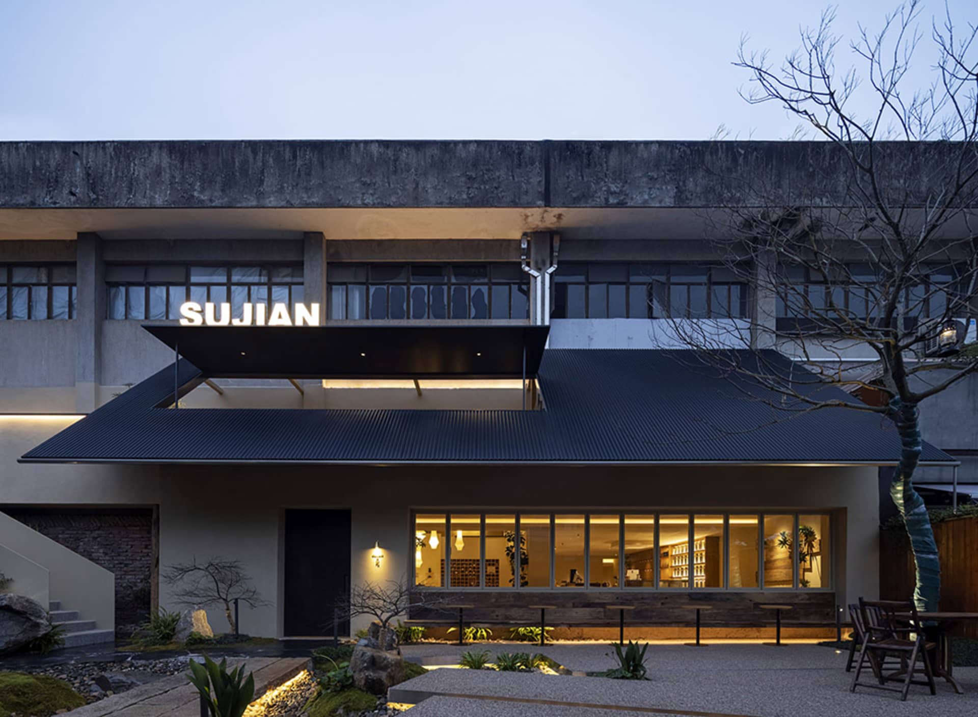 Modern building with a large roof overhang, featuring a mix of concrete, wood, and metal materials, with natural light entering through several windows