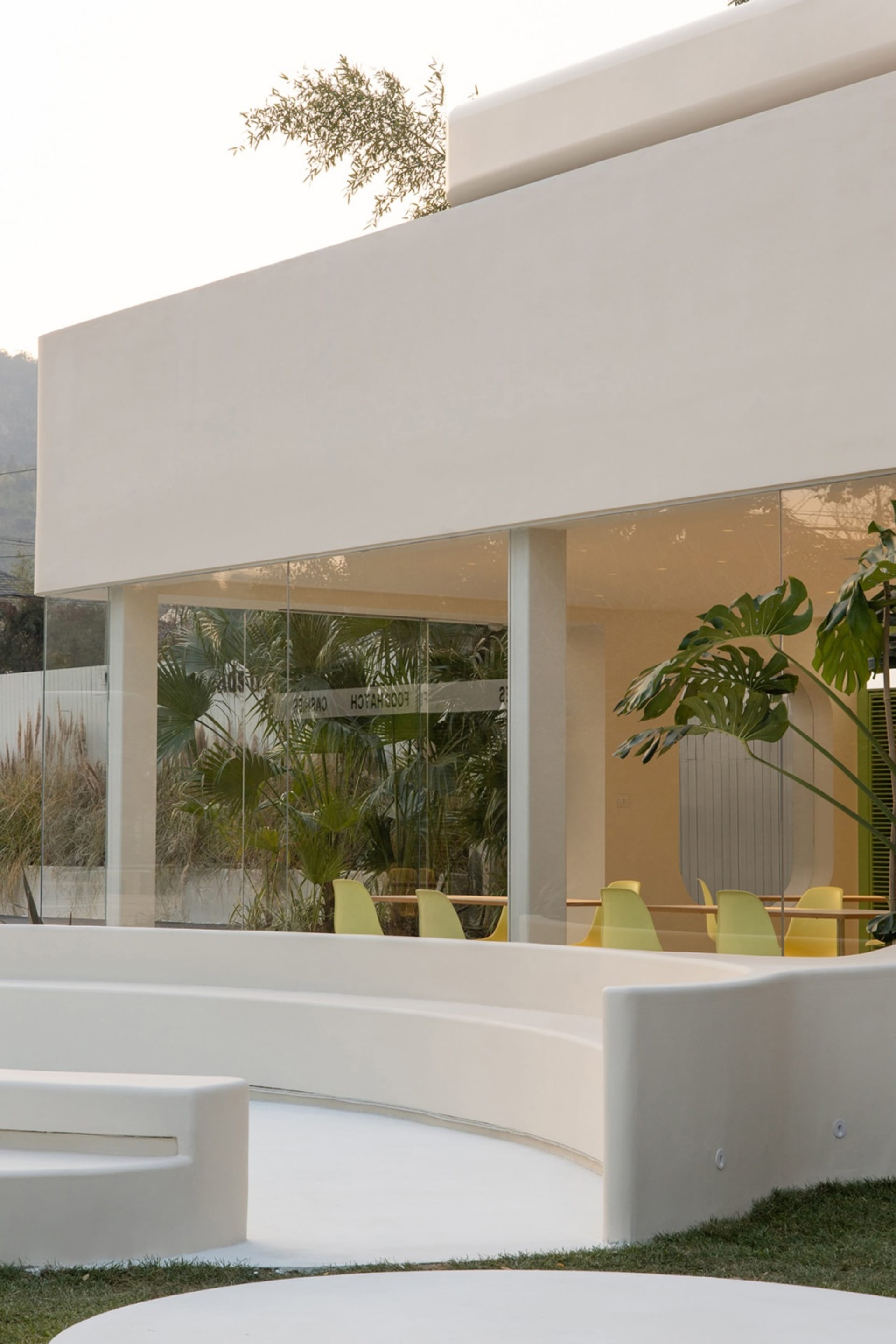 Inviting indoor space with a large white wall, glass doors, yellow chairs, and potted plants
