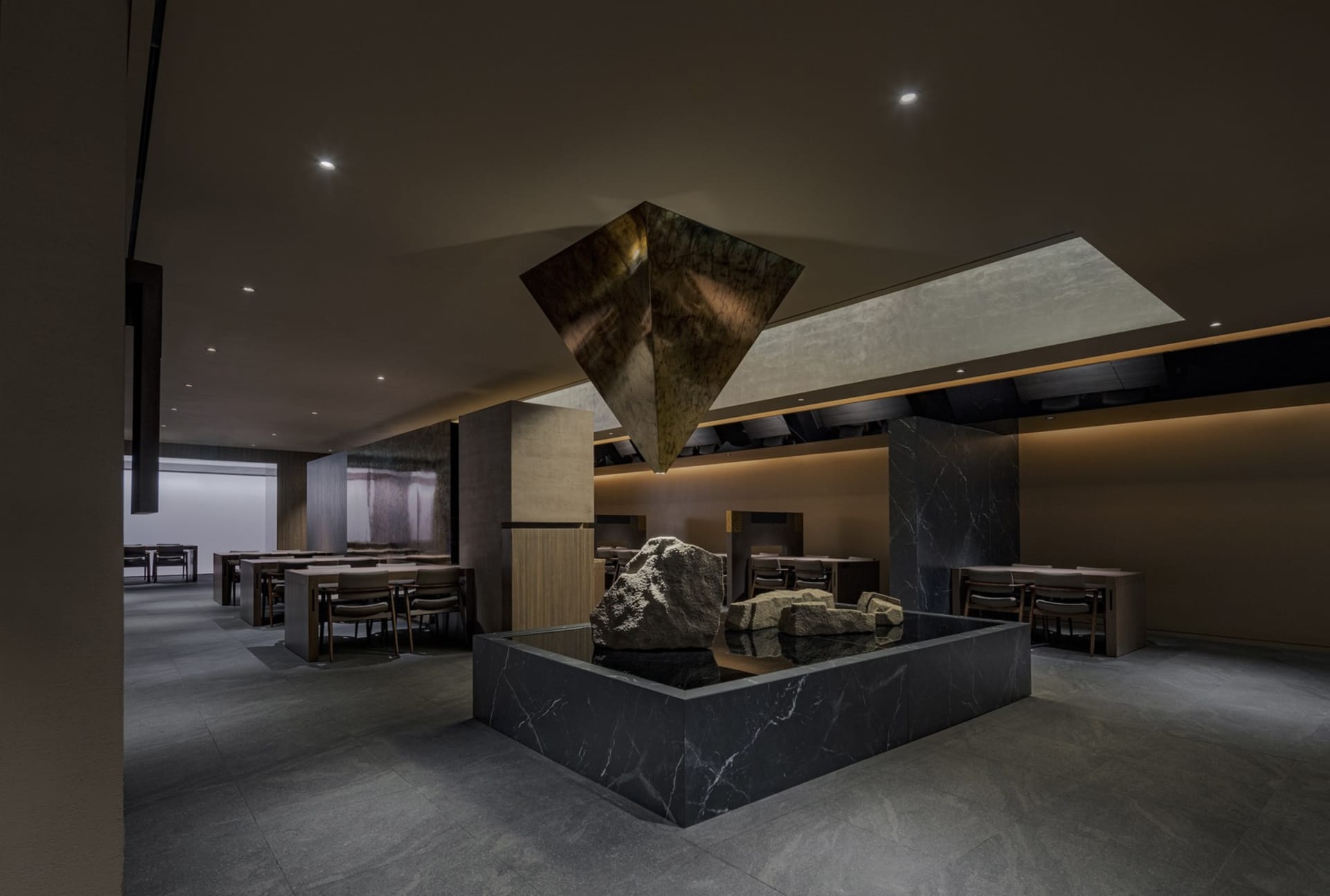 Dimly lit restaurant interior with a stone sculpture centerpiece, surrounded by tables and chairs, with a warm and earthy atmosphere