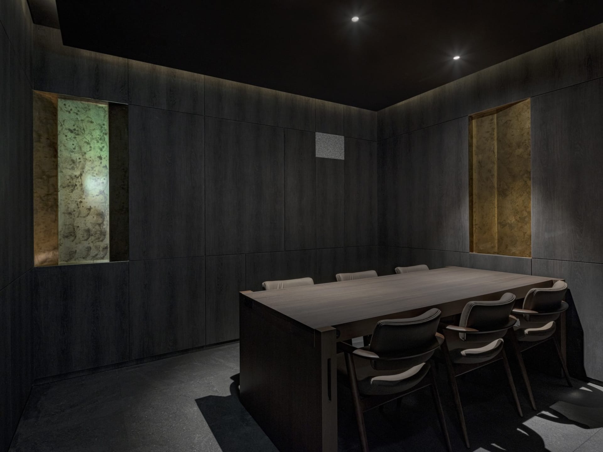 Dimly lit office space with a wooden table surrounded by four chairs, occupying most of the room's width