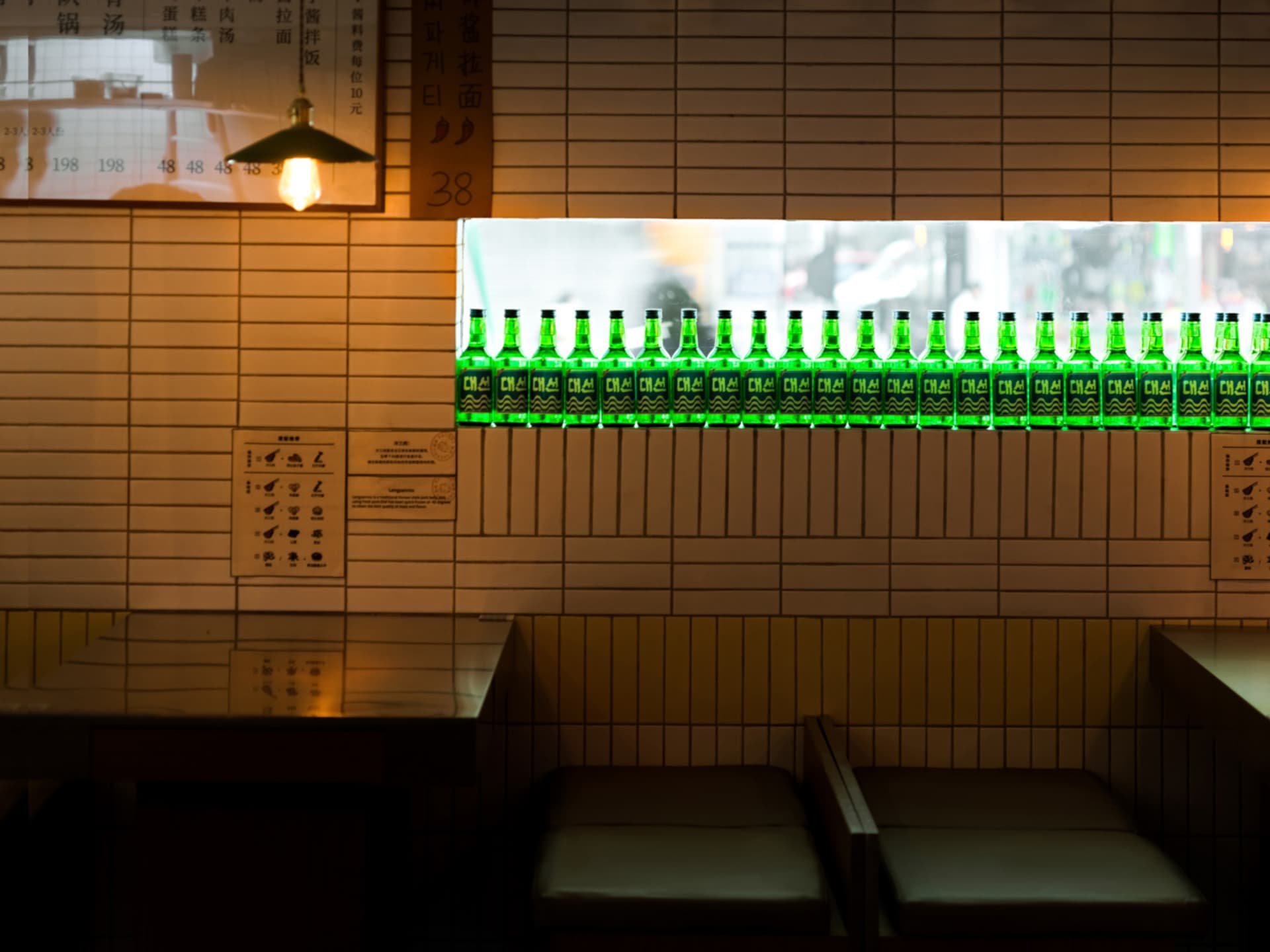 A cozy bar area in an Asian restaurant with a brick wall, green bottles, and comfortable seating for patrons