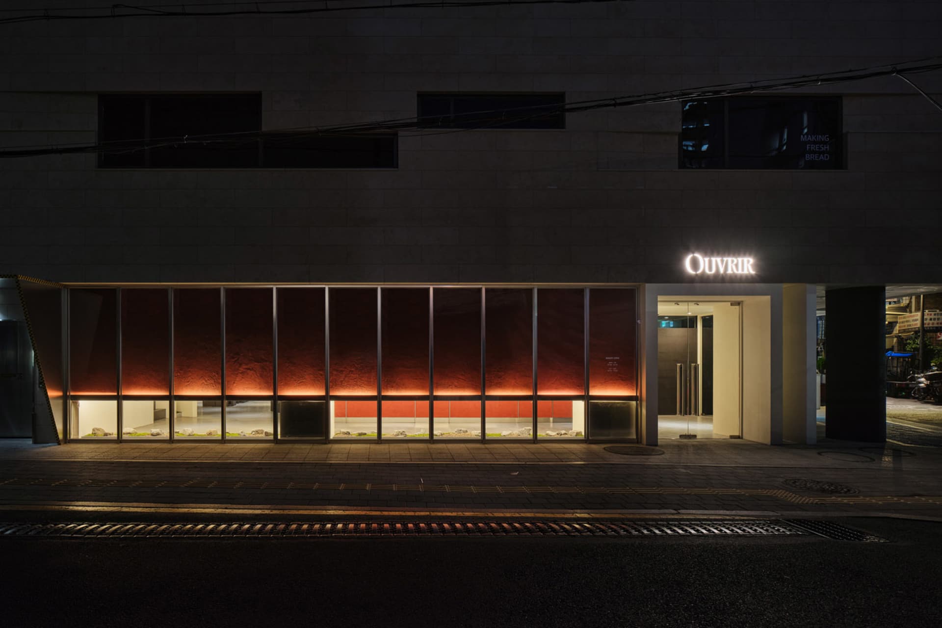 A modern building at night with a large window display in front of a store, featuring a prominent red wall against a dark background