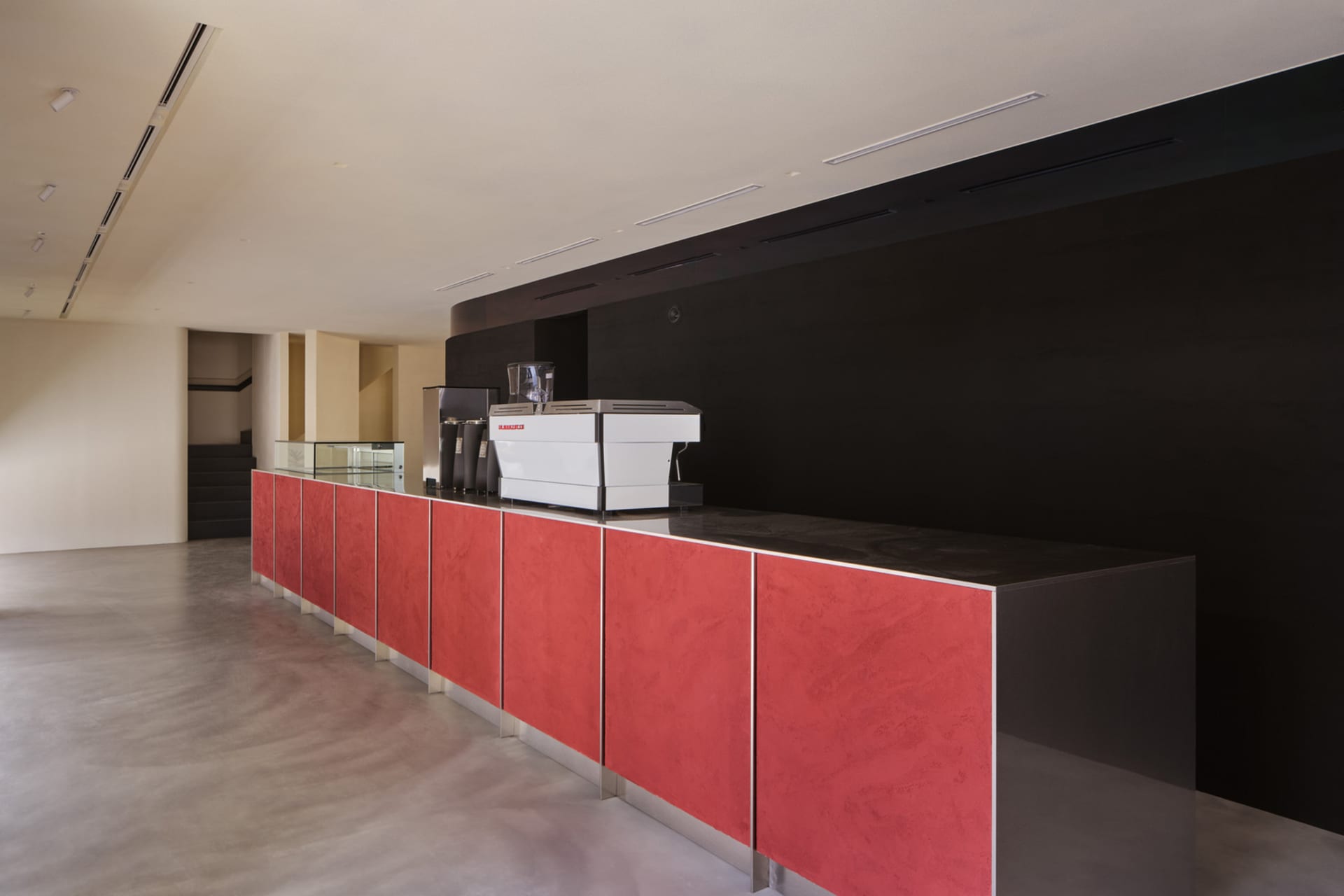 A cozy coffee shop interior with a red countertop, a large coffee machine, and several cups, creating a warm atmosphere