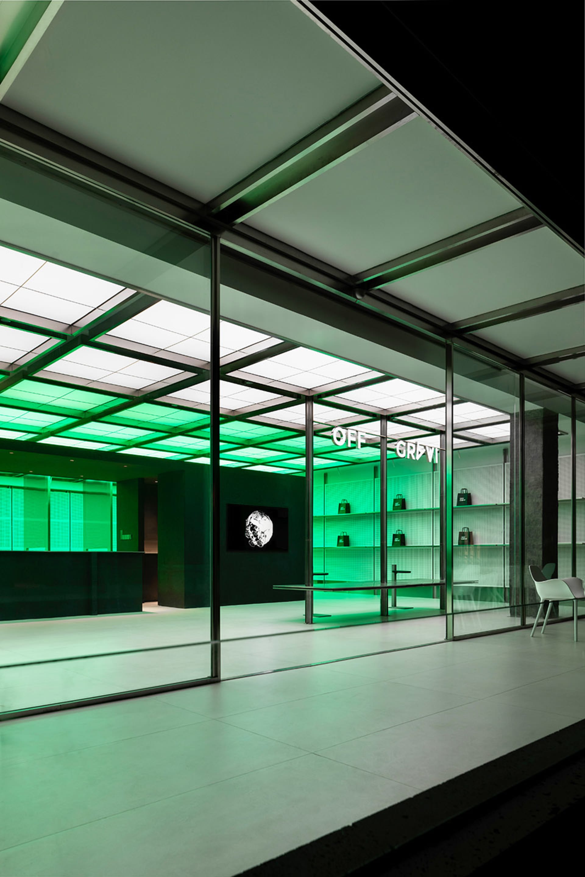 Office space with green walls, a large glass window, two chairs, a mounted TV, and scattered books, creating a modern and inviting atmosphere