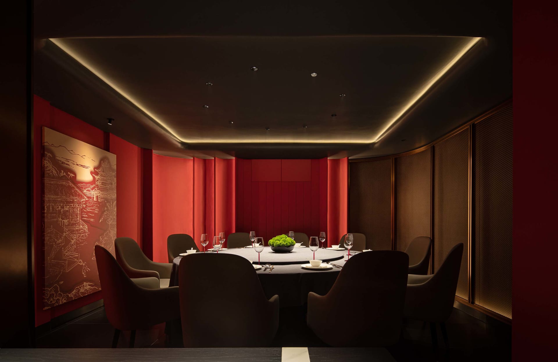 A luxurious dining area with a round table, wine glasses, plates, and cutlery, surrounded by multiple chairs in a warm and cozy red-themed space