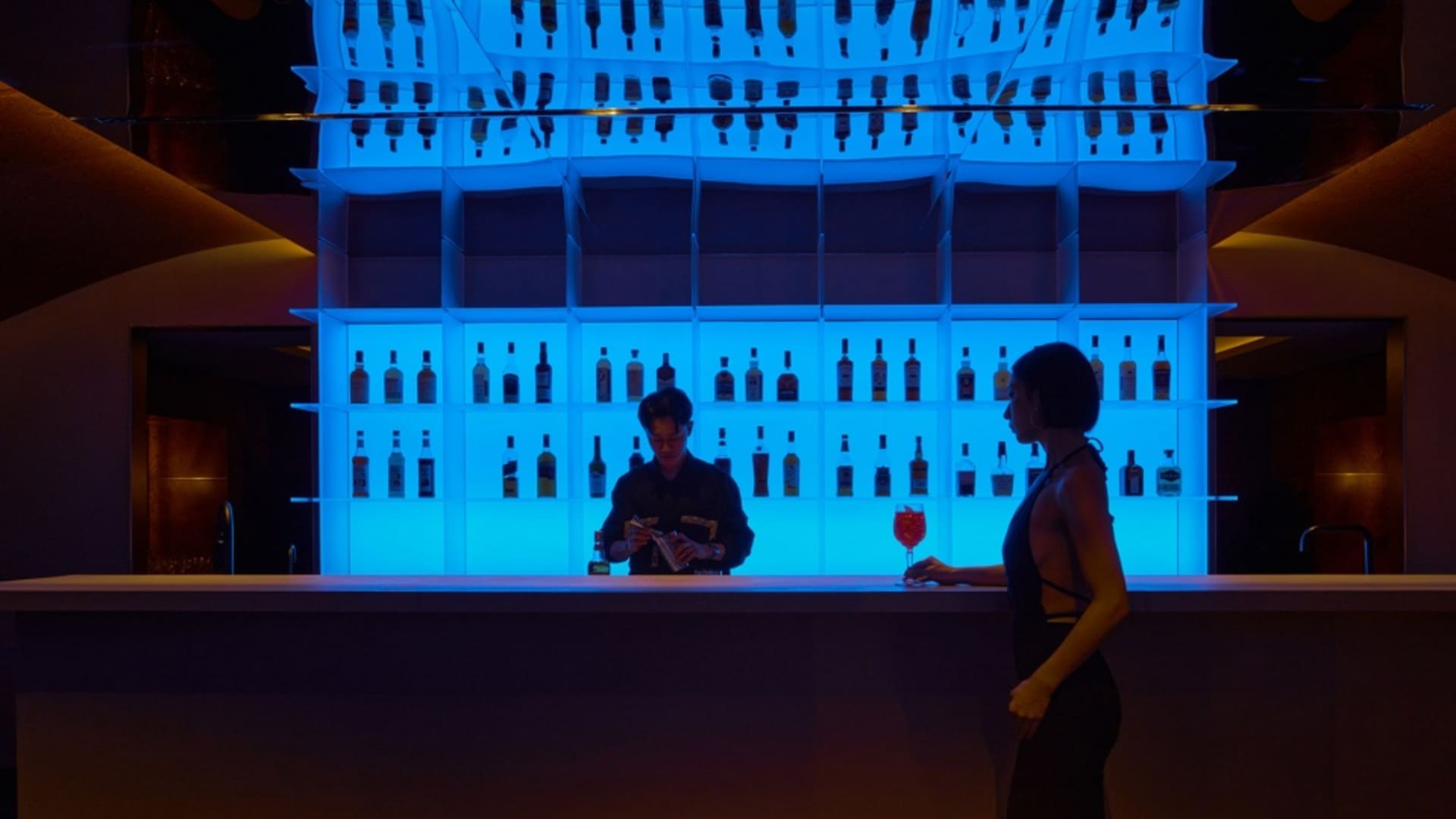 熱鬧酒吧場景，調酒師為顧客調製飲品，周圍環繞瓶裝酒與玻璃杯，營造溫暖社交氛圍
