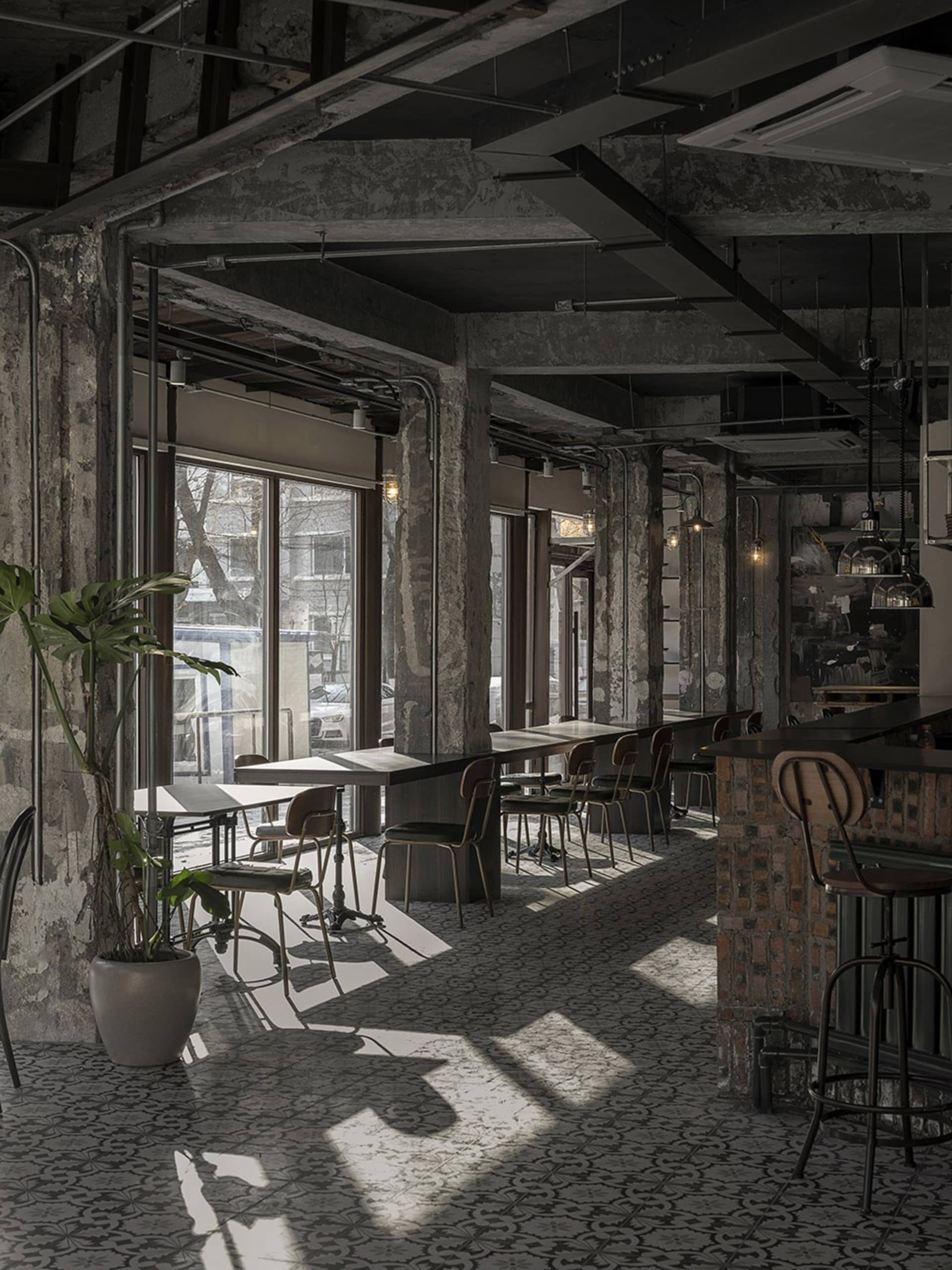 Empty restaurant interior with brick walls, dining tables, and chairs, flooded with natural light through a large window