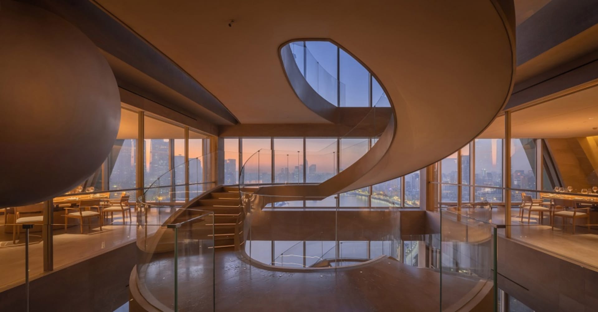A large building with multiple levels, glass walls, and a wooden staircase, allowing natural light to enter and creating a bright atmosphere
