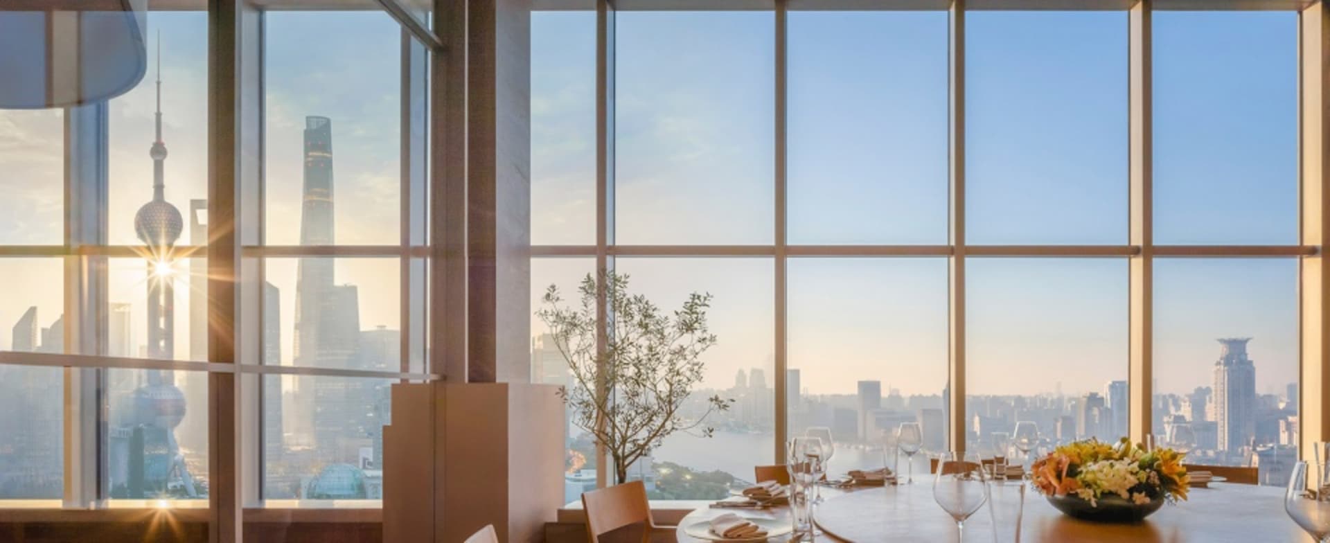 Modern dining area with chairs around a table, wine glasses, and a large window offering a city skyline view