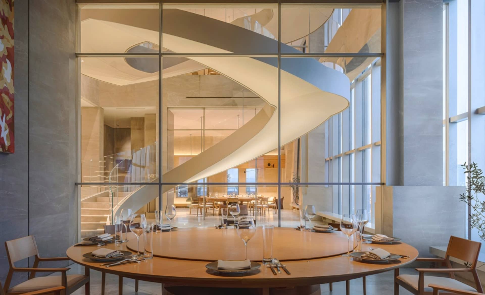 Sophisticated restaurant interior with a wooden spiral staircase, metal railing, and multiple tables and chairs