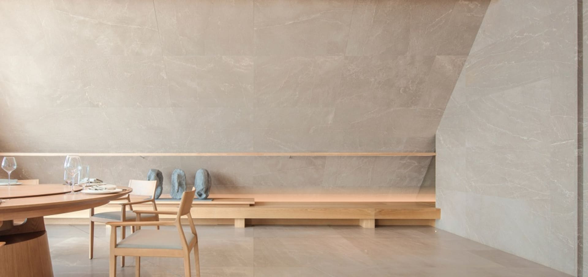 Empty room with a stone wall, a wooden bench, two chairs, and decorative vases, creating a calm and serene atmosphere