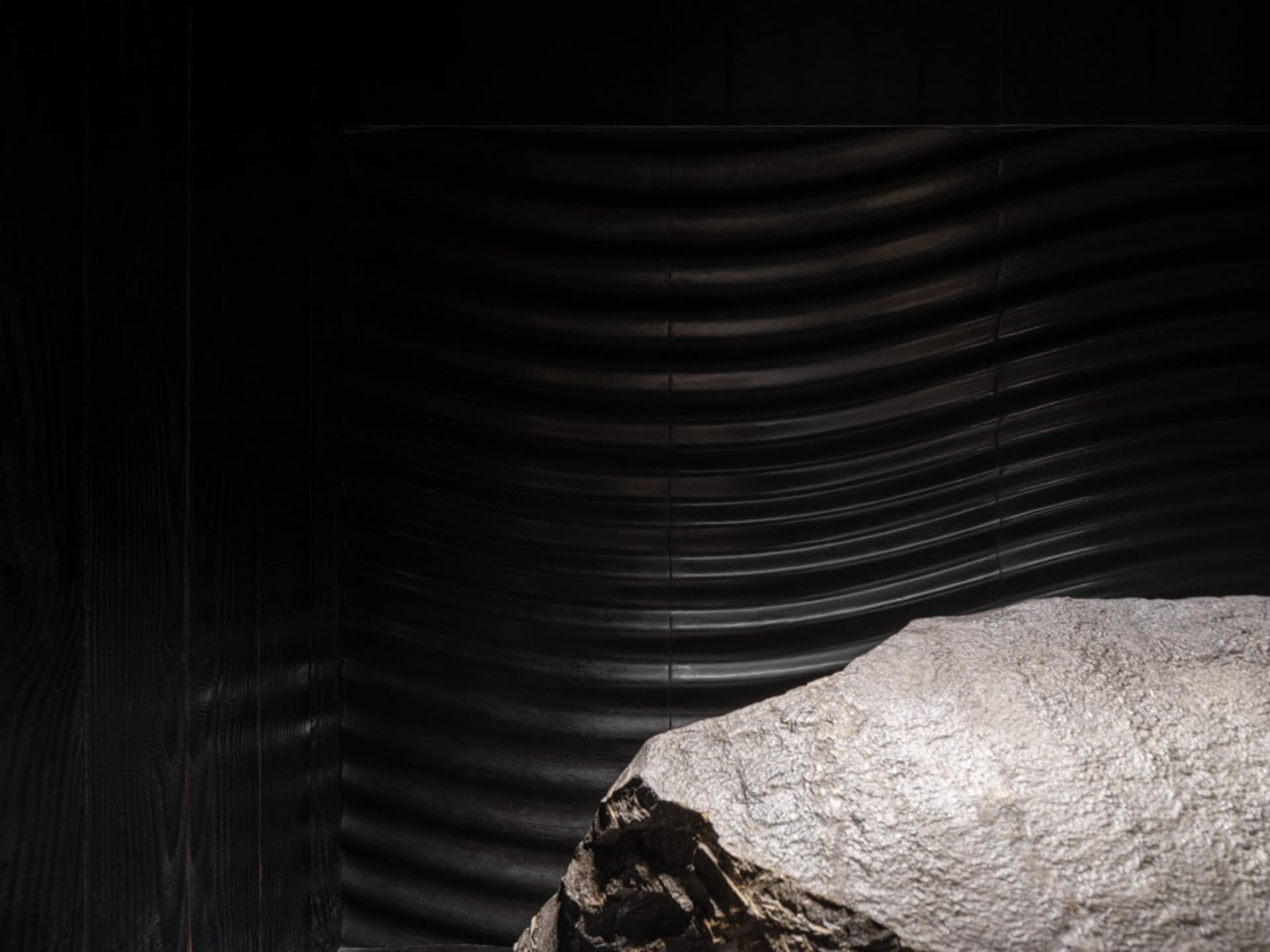 A dark and moody interior space with a large rock at its center, surrounded by black walls and no other objects or people