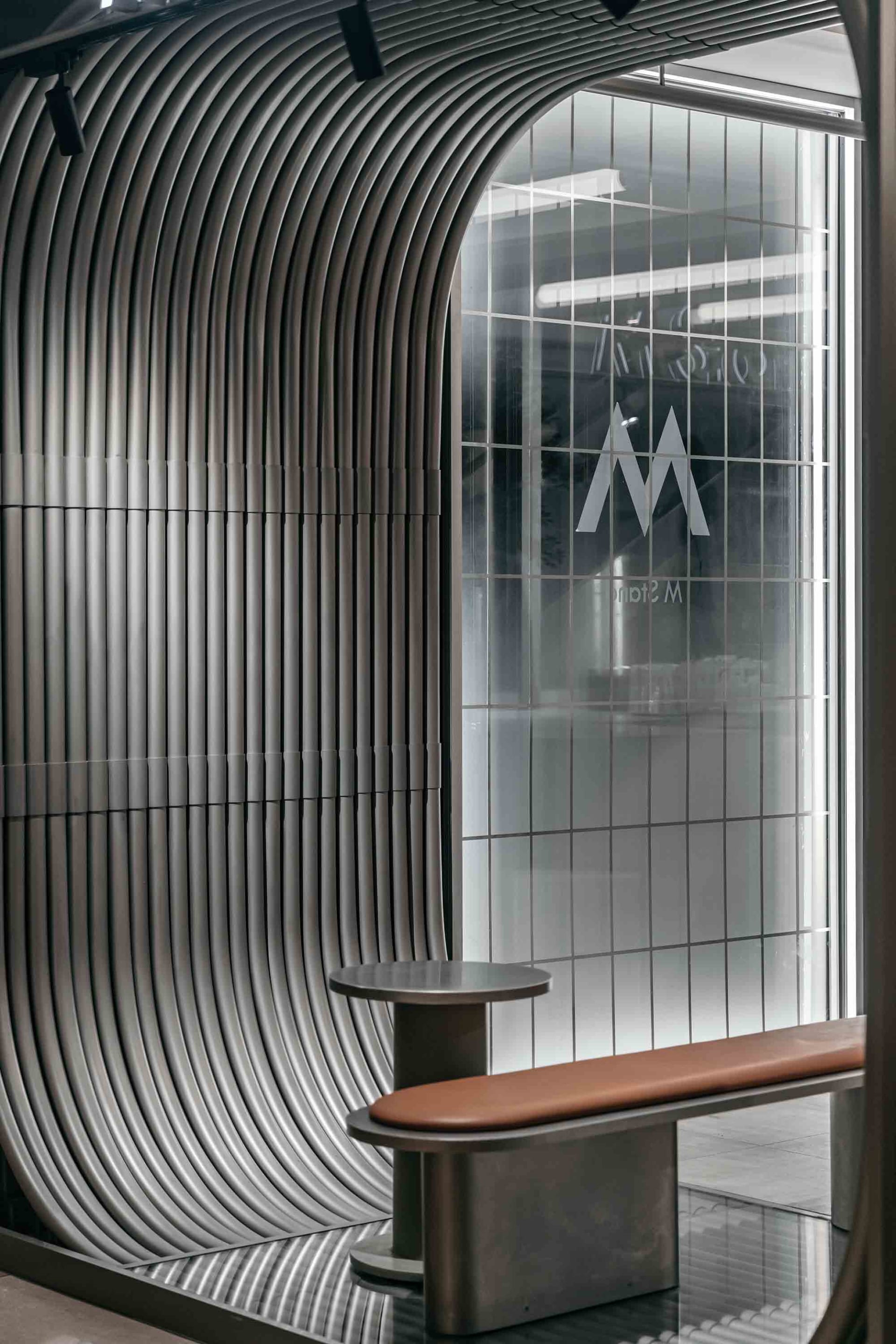 A modern interior design featuring a wooden and metal bench in front of a glass wall with a logo, set against a neutral background