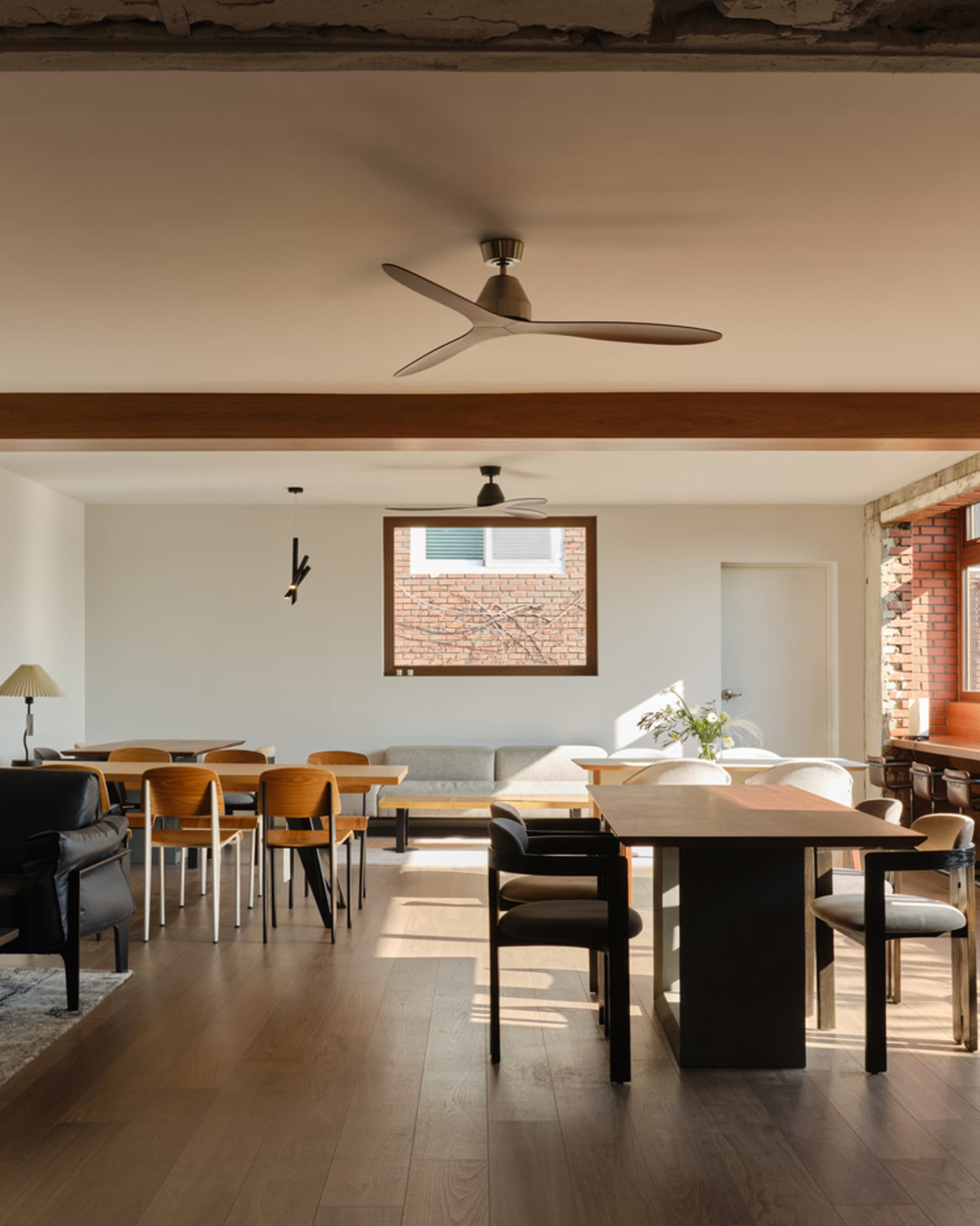 A modern living room with wooden floors and walls, featuring a dining table, chairs, kitchenette, and a potted plant, with a modern and stylish design