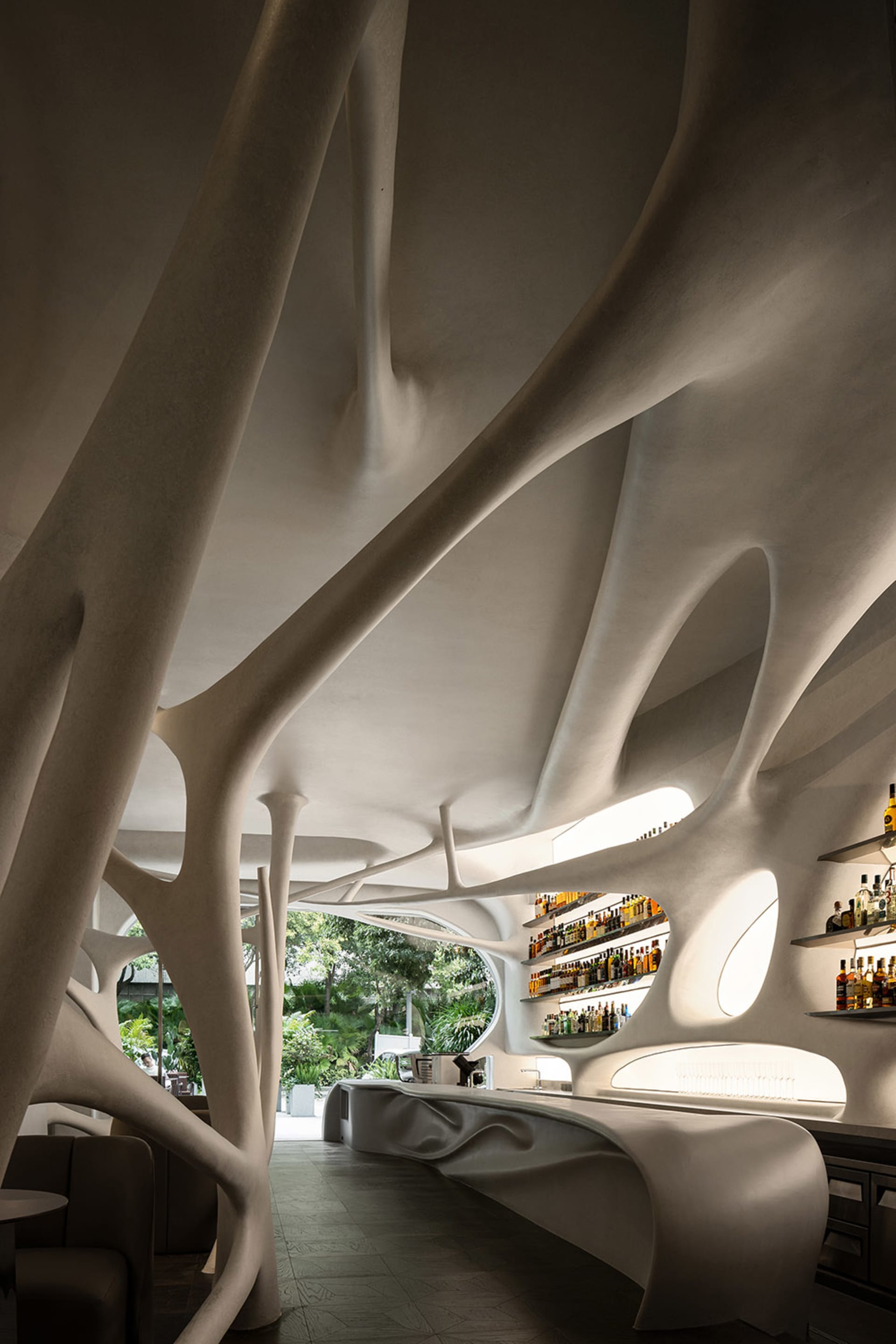 Modern bar area with a unique tree branch design on a white wall, bottles on display, and a comfortable atmosphere