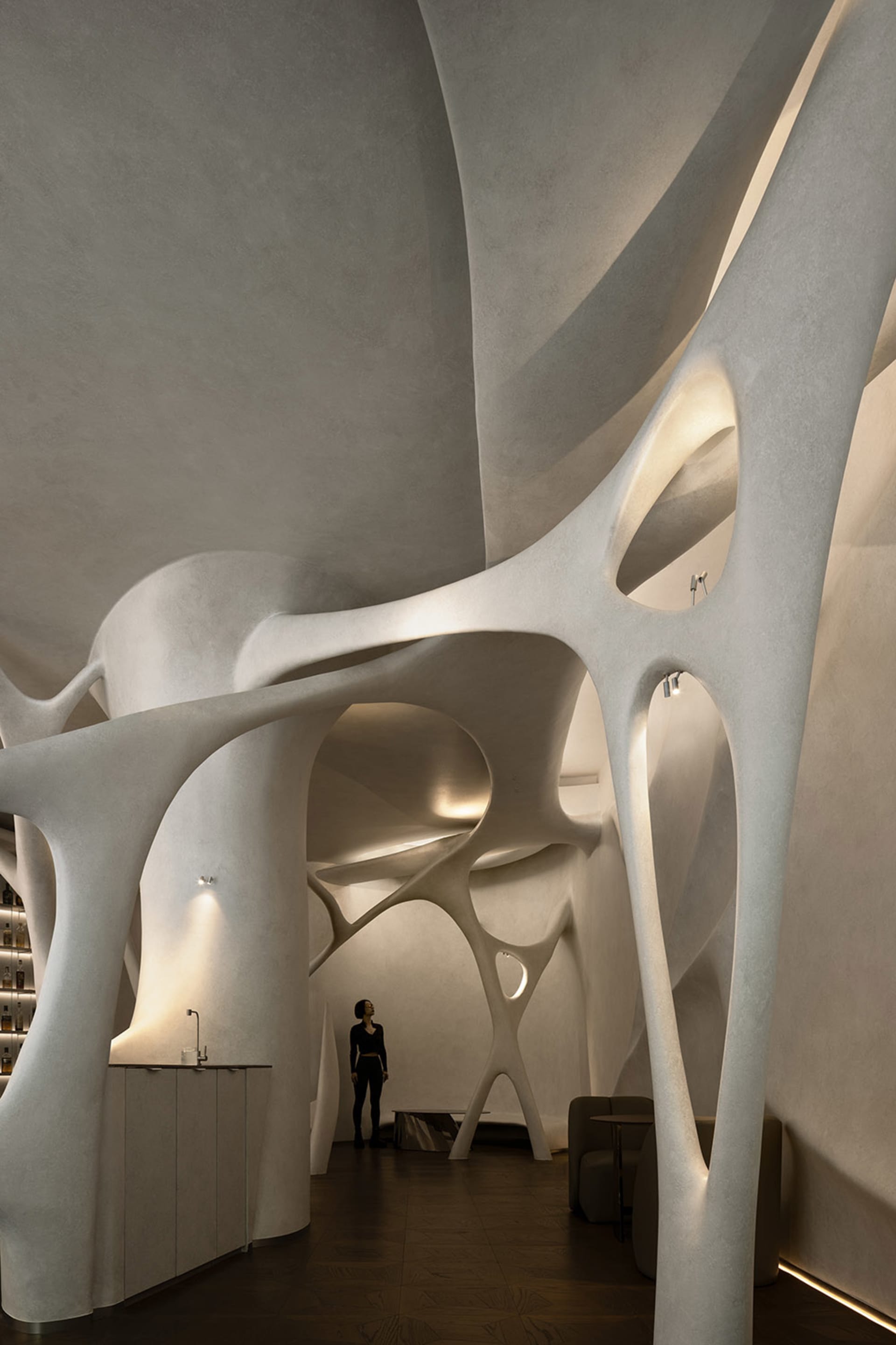 A modern art gallery with curved white walls and ceilings, featuring two people observing exhibits in a dimly lit space